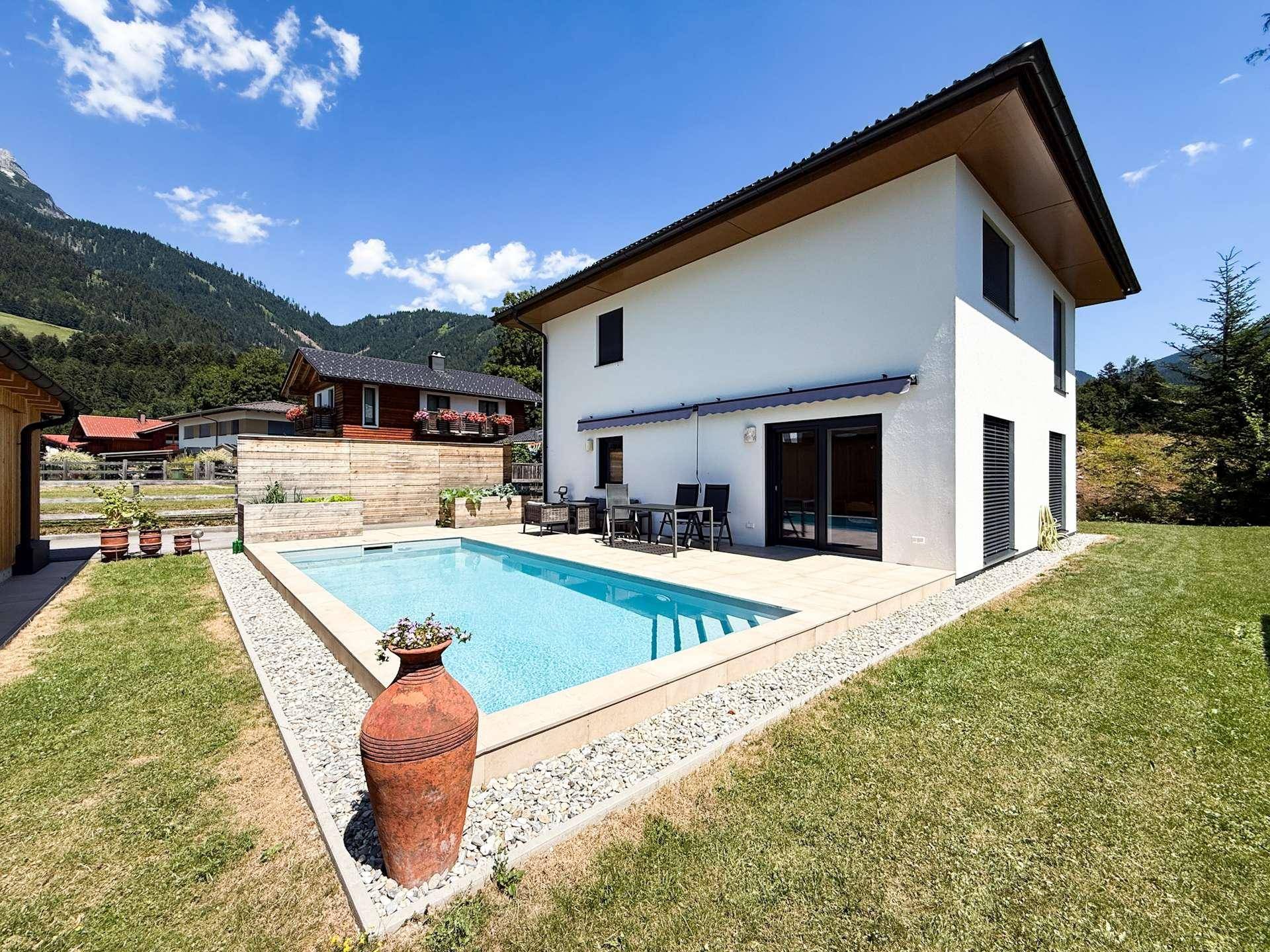 Sonniger Gartenbereich mit erfrischendem Pool, Terrasse und beeindruckendem Bergblick.