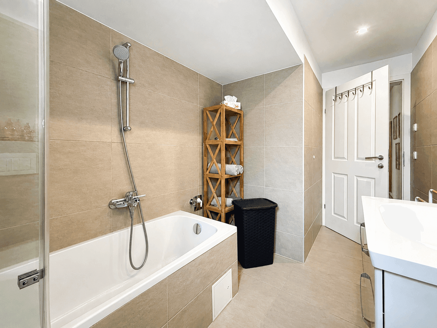 Helles Badezimmer mit Badewanne, Duschfunktion und beigefarbenen Wand- und Bodenfliesen.