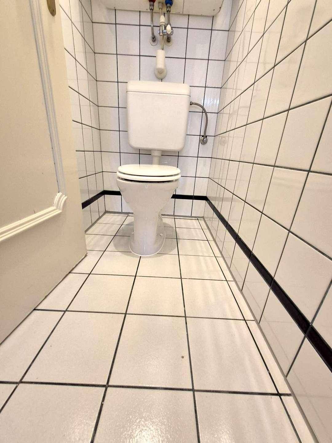 Separate Toilette mit weißen Fliesen und klassischem WC, sauber und praktisch.