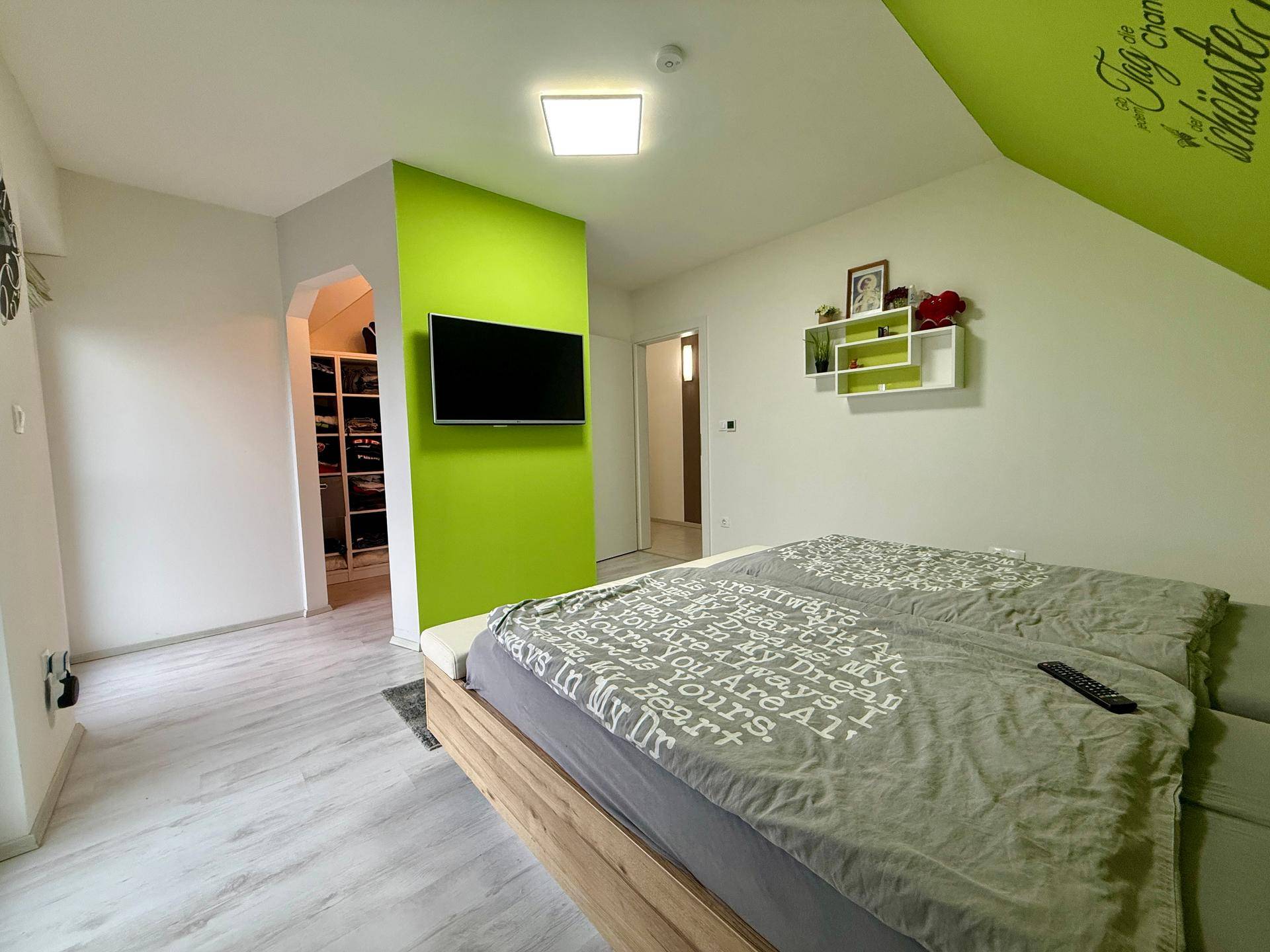 Geräumiges Schlafzimmer mit Doppelbett, grüner Wand und begehbarem Kleiderschrank.