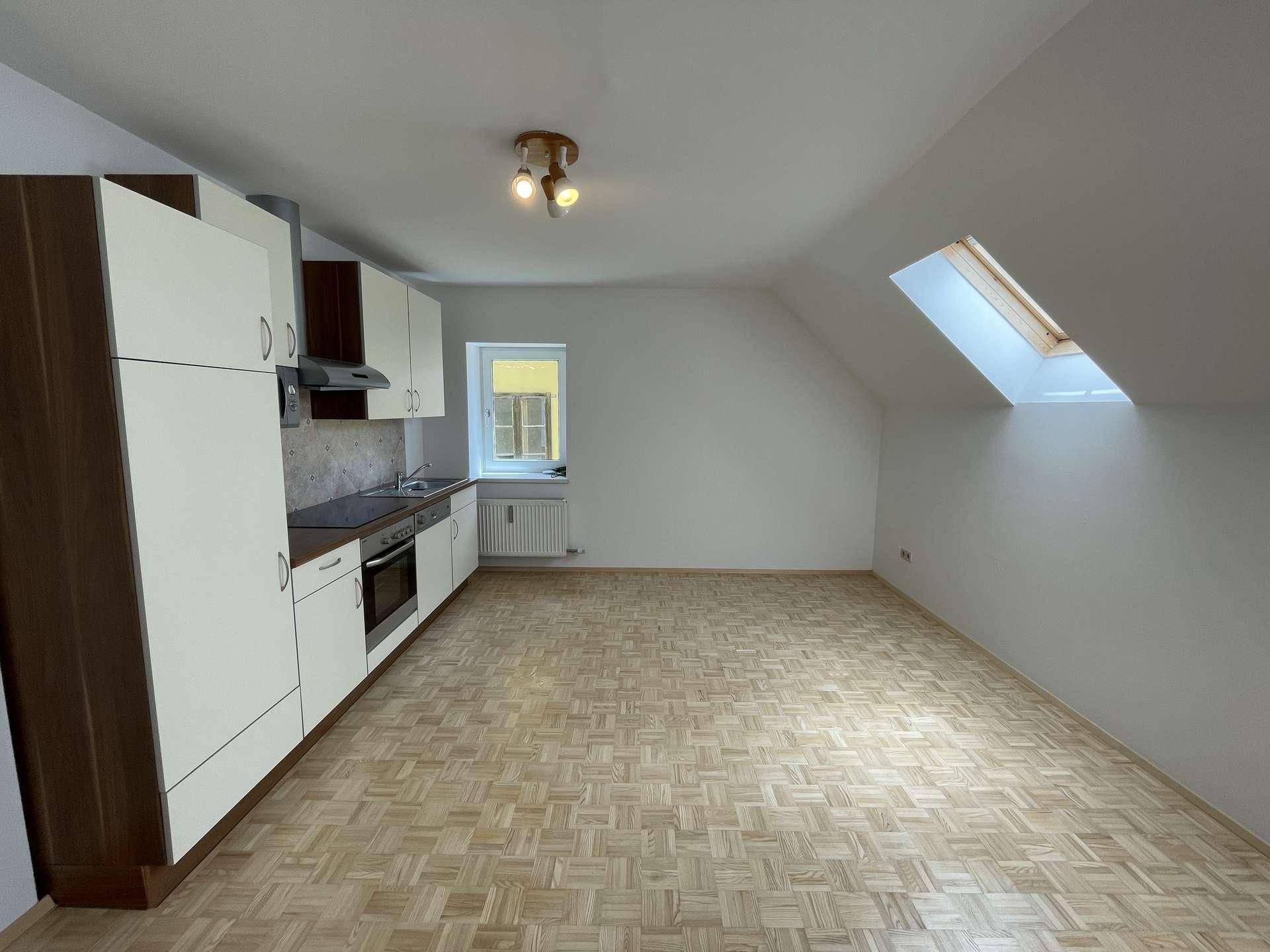 Offener Wohnbereich mit Küchenzeile, Parkettboden und Dachschrägenfenster.