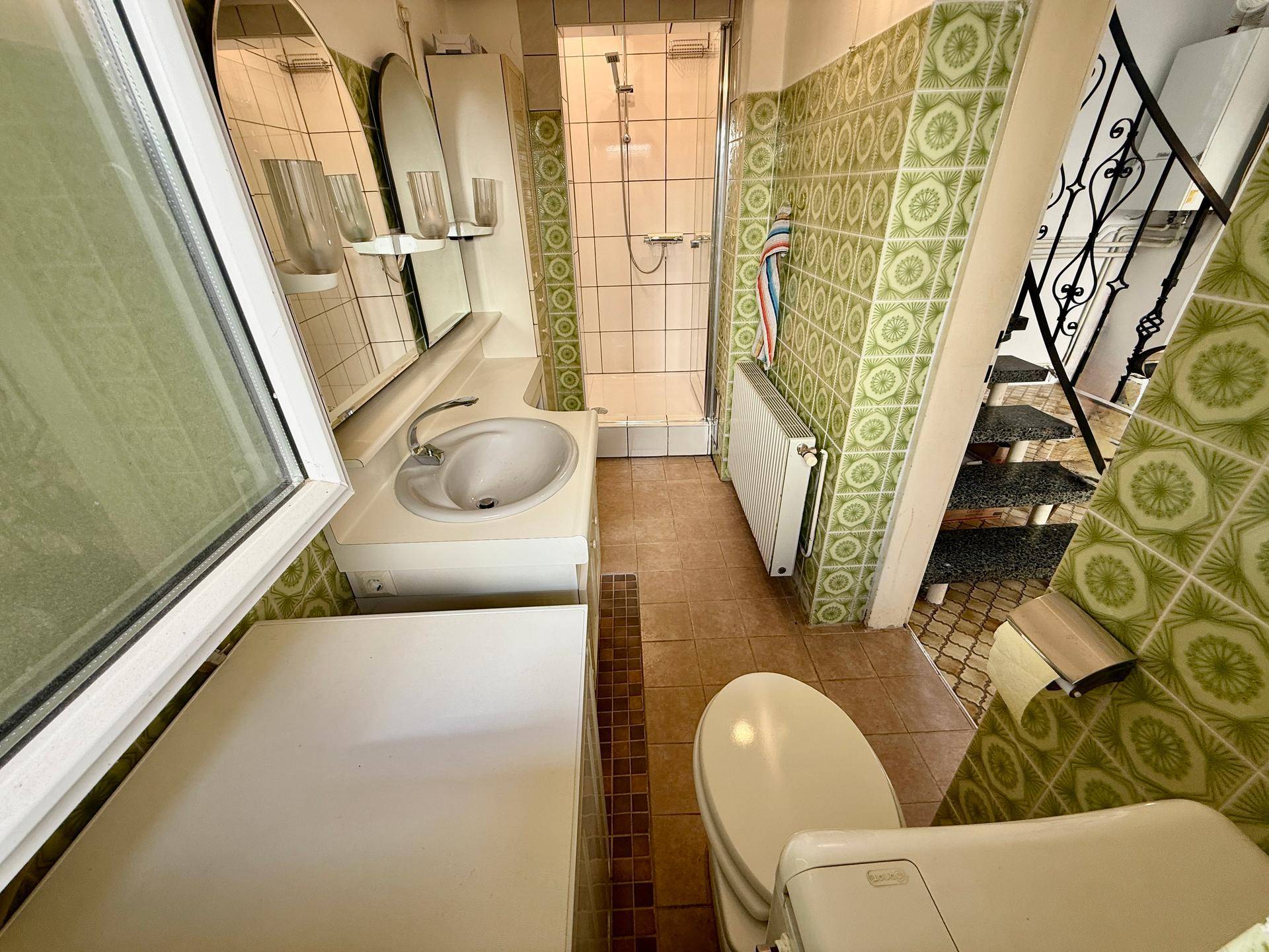 Badezimmer mit Duschkabine, Waschbecken und einem Fenster.