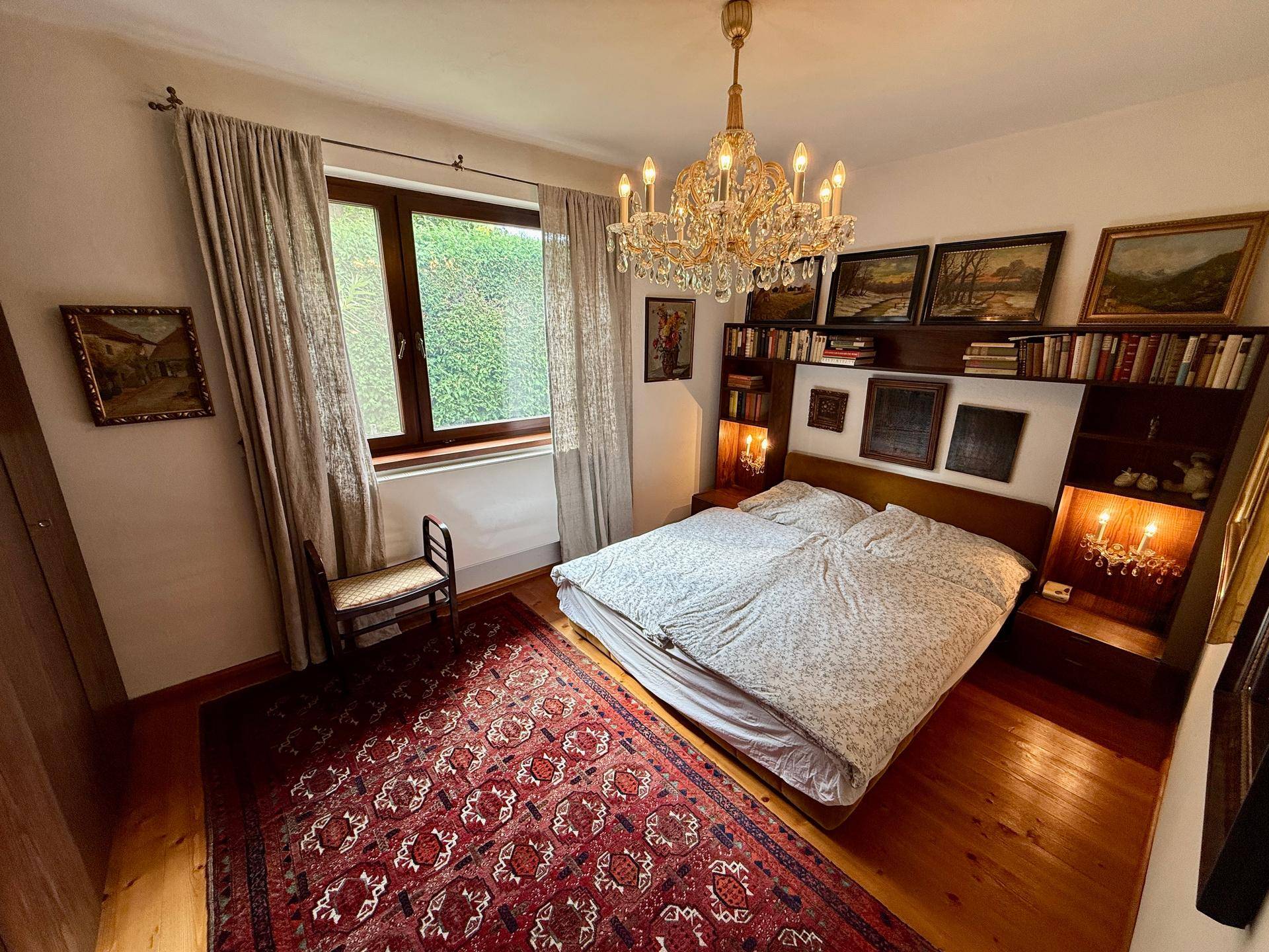 Geräumiges Schlafzimmer mit Doppelbett, Bücherregal, Kronleuchter und Holzboden.