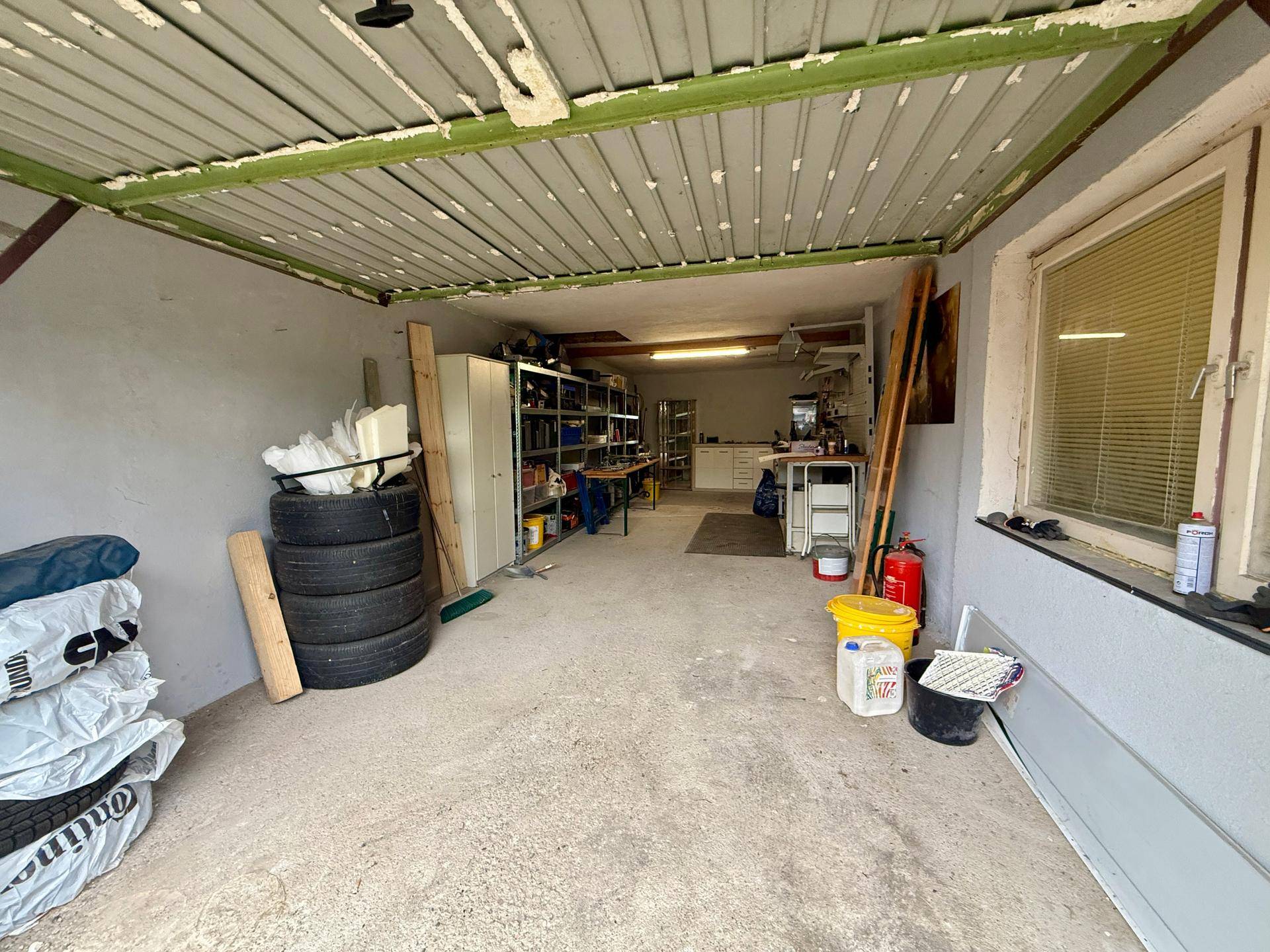 Geräumige Garage mit Betonboden, Regalen und Lagerfläche für Reifen und Werkzeuge.
