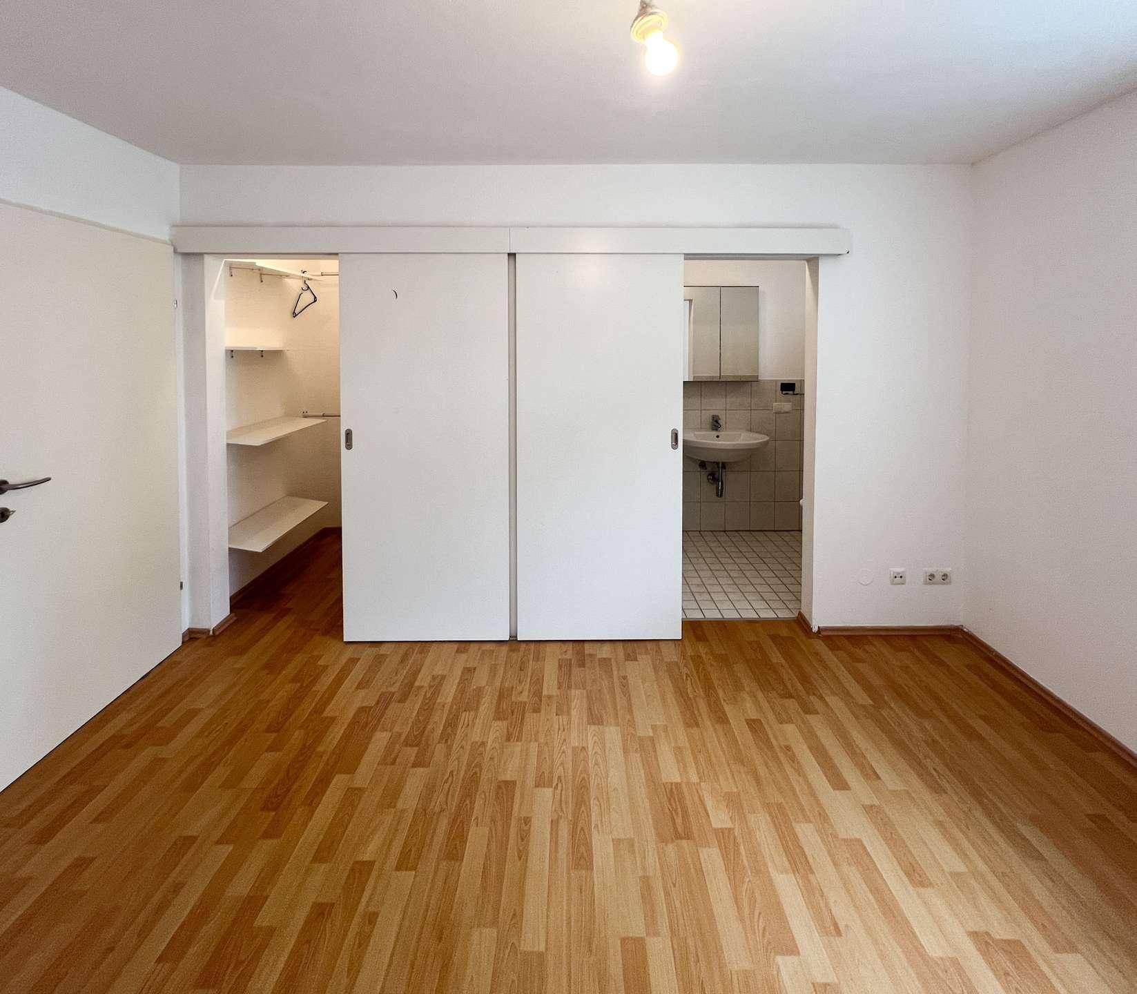 Schlafzimmer mit Laminatboden, Schiebetüren zu Bad und begehbarem Kleiderschrank.