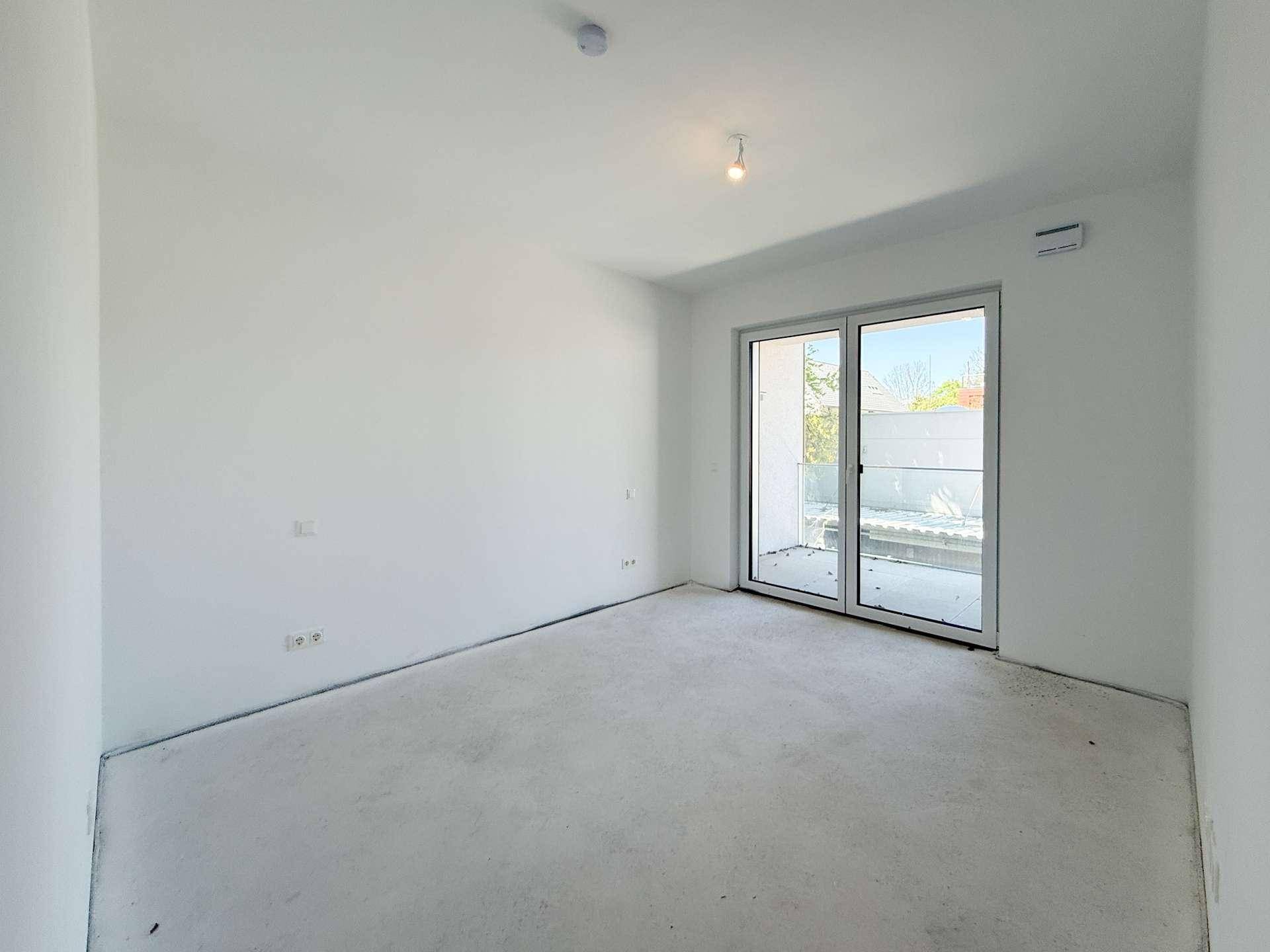Helles Schlafzimmer im Rohbau mit Schiebetür zu einem Außenbereich.