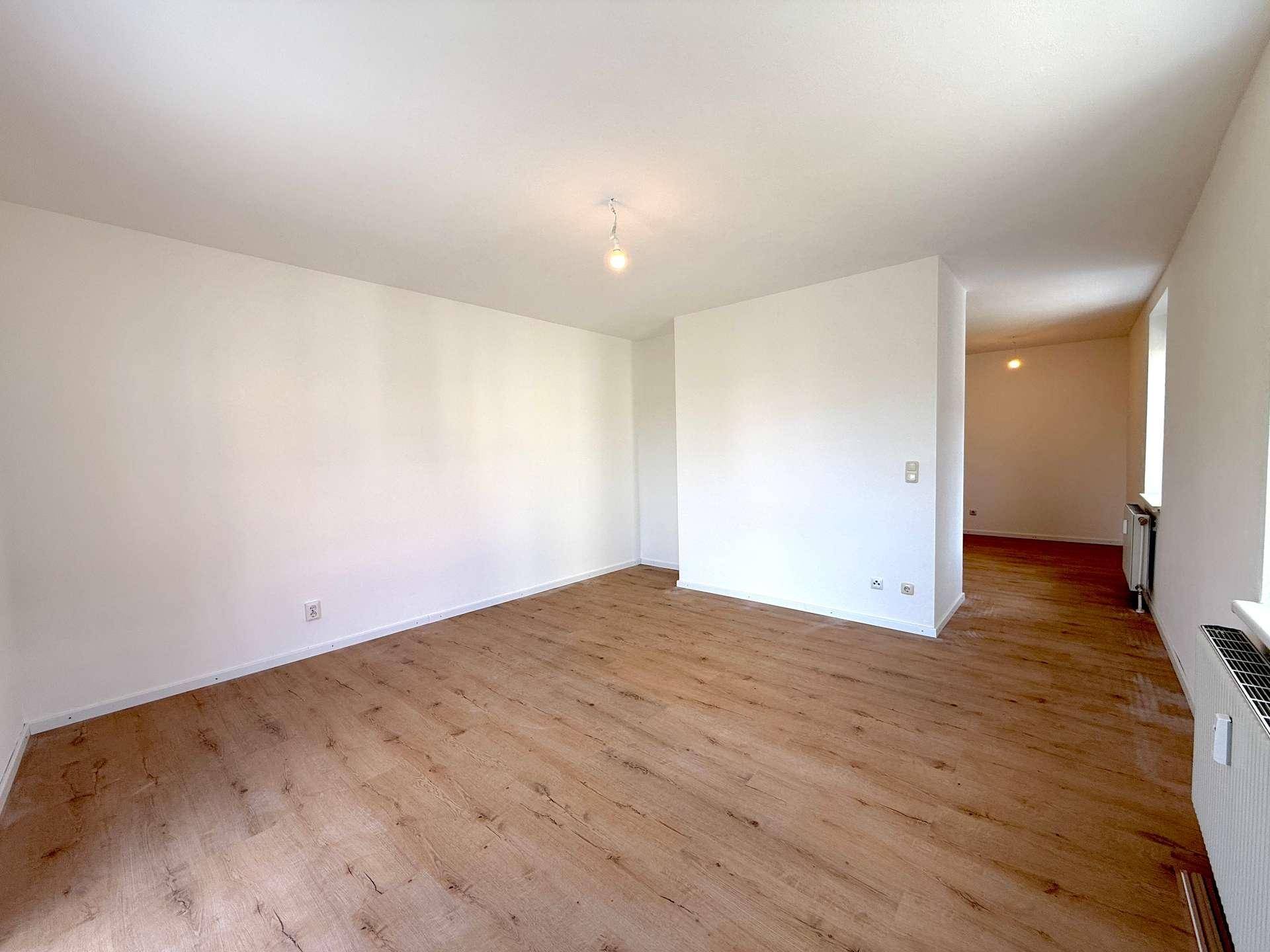 Geräumiger, heller Raum mit Laminatboden und Blick in einen weiteren Bereich der Wohnung.