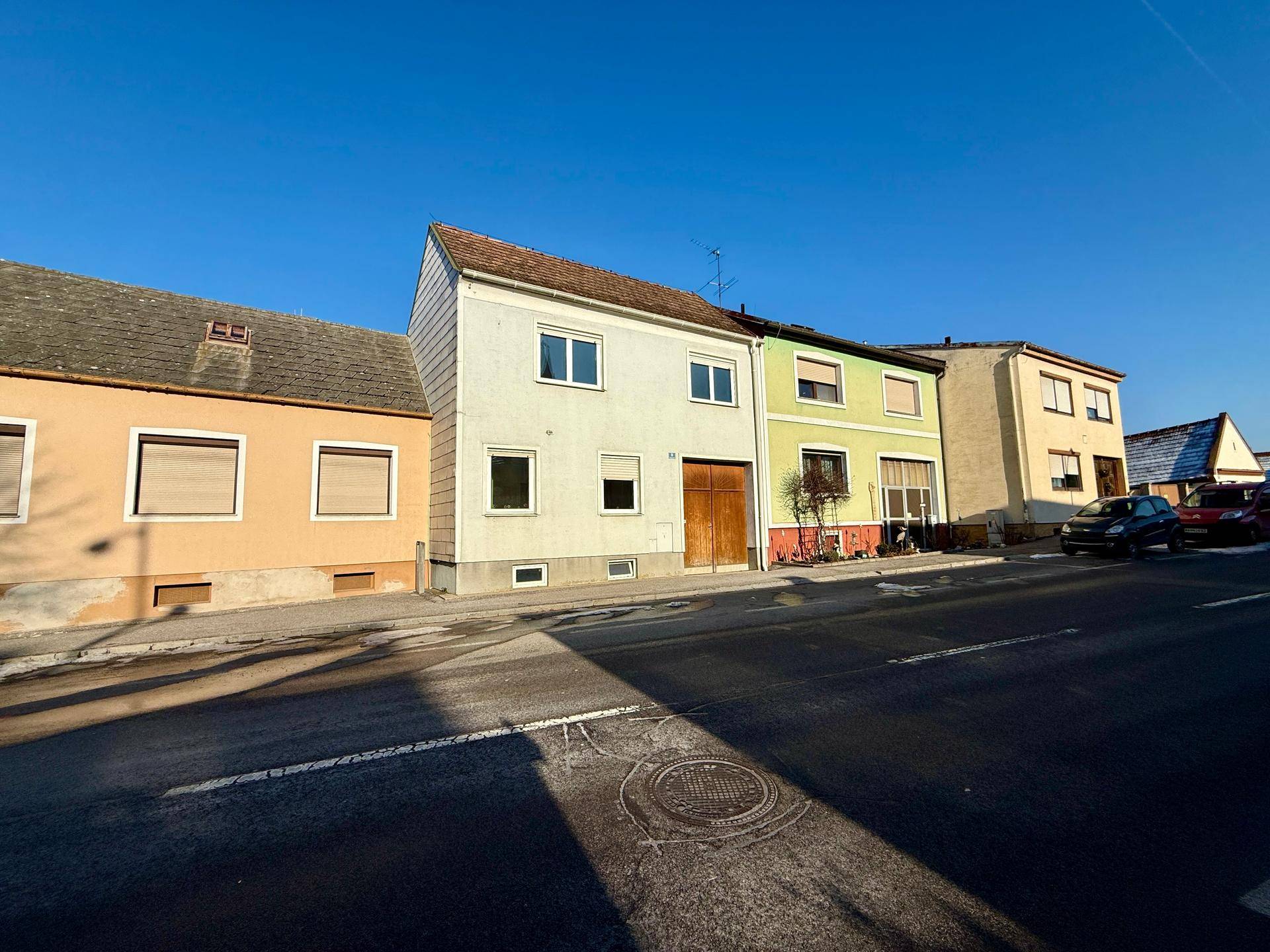 Reihenhausfassade an einer sonnigen Straße mit geparkten Autos.
