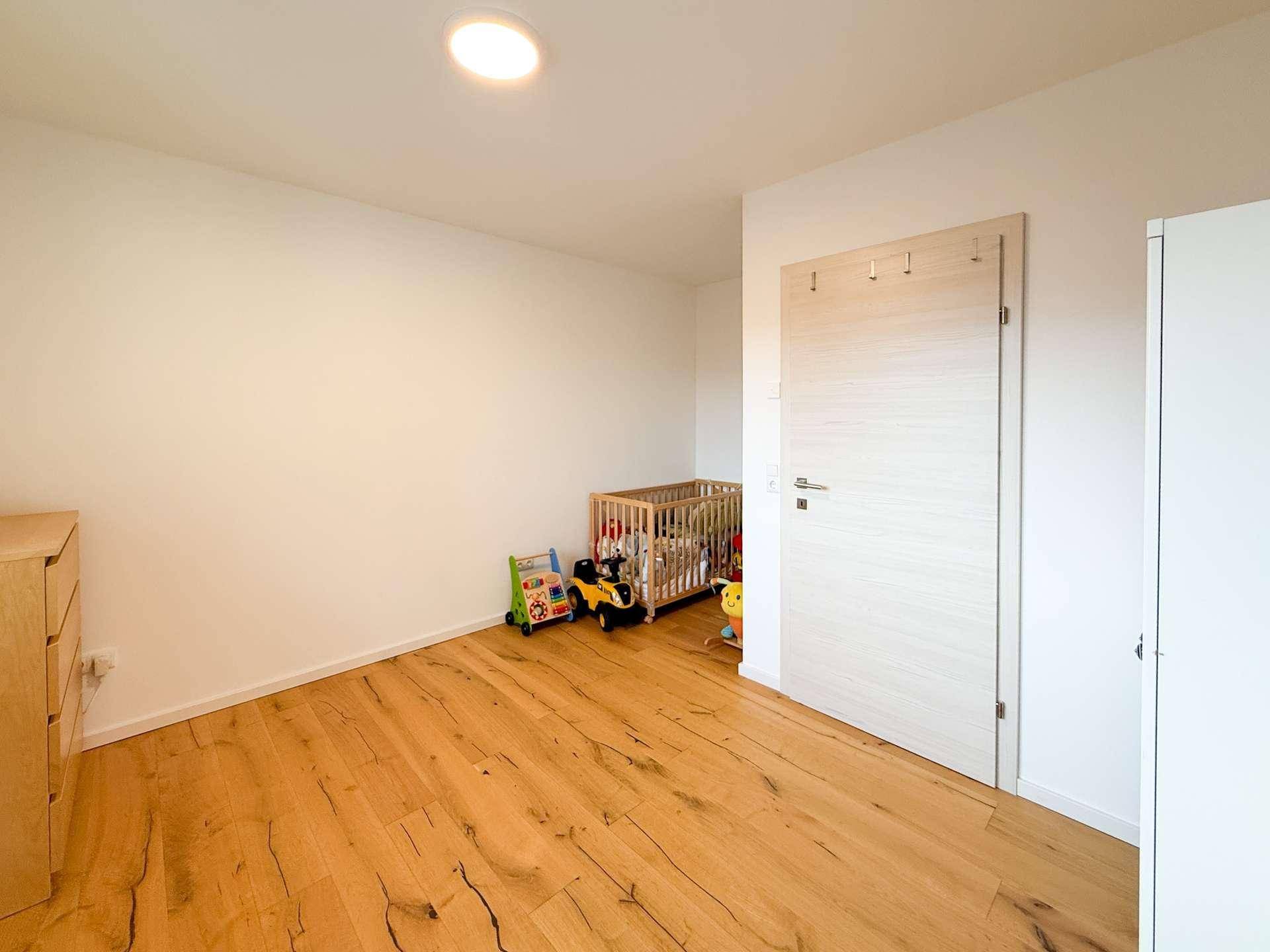 Kinderzimmer mit Holzboden, Babybett und viel Platz zum Spielen.