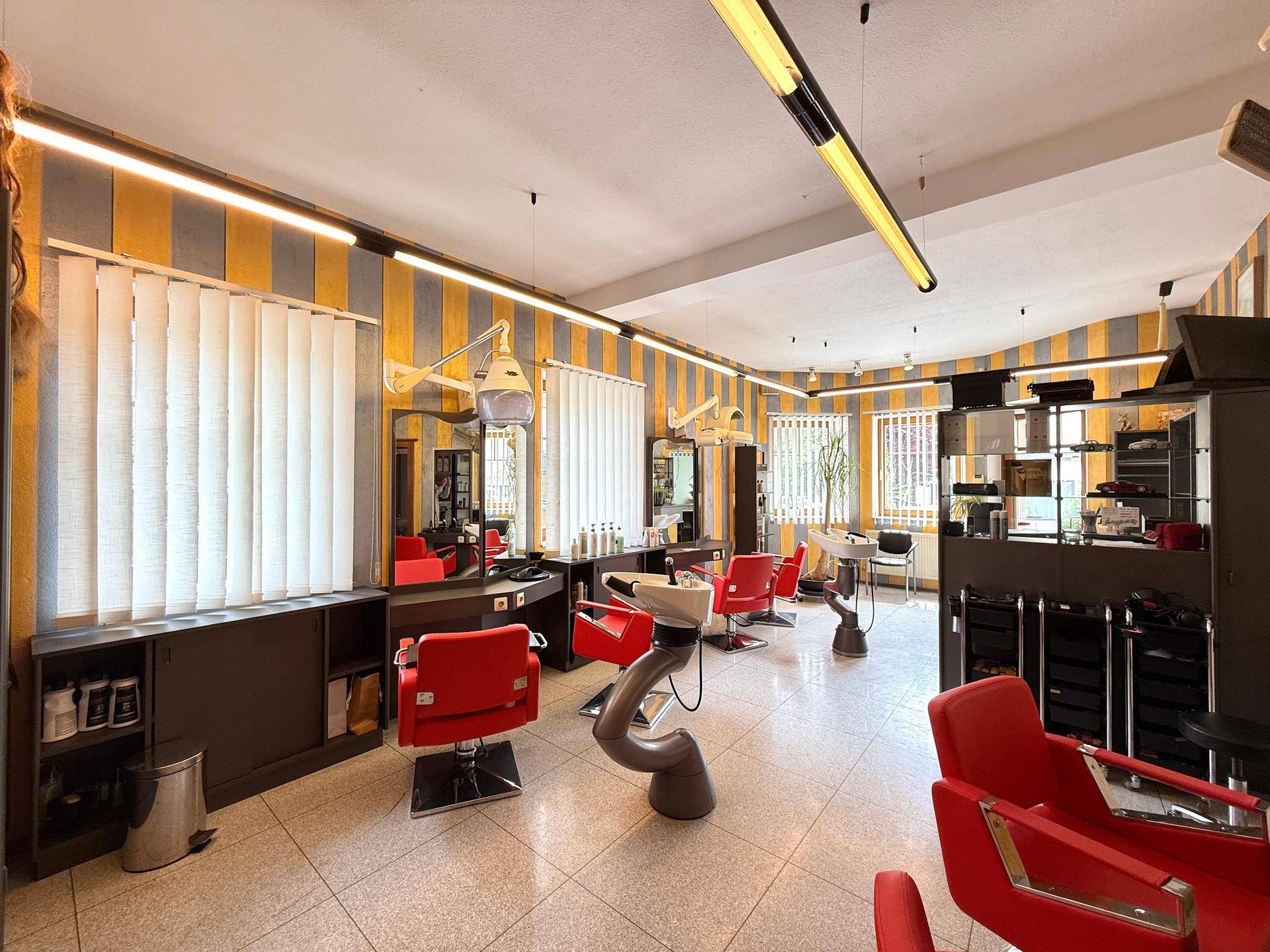 Moderner Friseursalon mit roten Stühlen, gestreiften Wänden und professioneller Ausstattung.