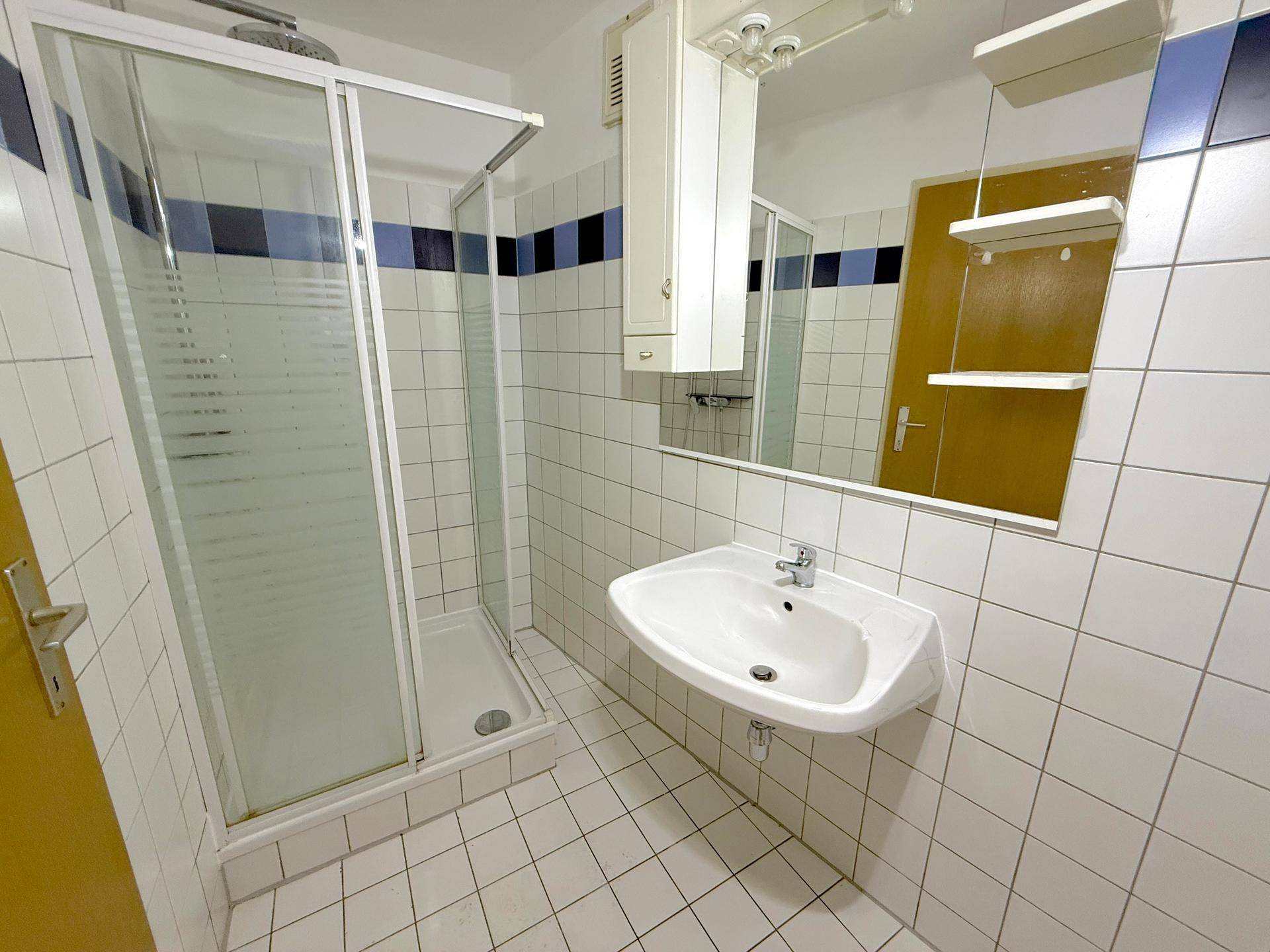 Badezimmer mit Duschkabine, Waschbecken und weißen Fliesen, teilweise mit blauen Akzenten.