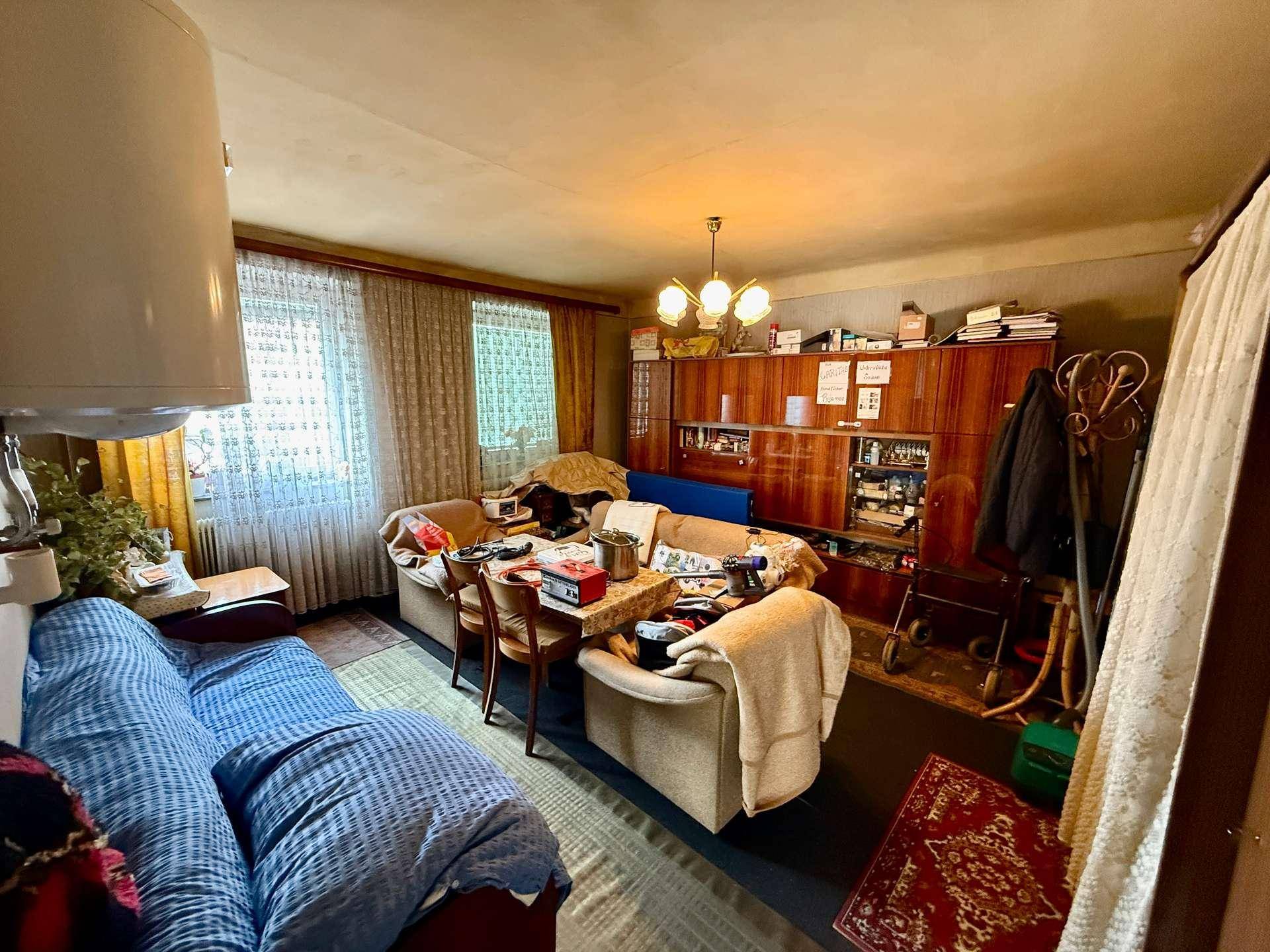 Gemütliches Wohnzimmer mit Sofa, Esstisch und traditionellen Holzmöbeln, in älterem Stil.