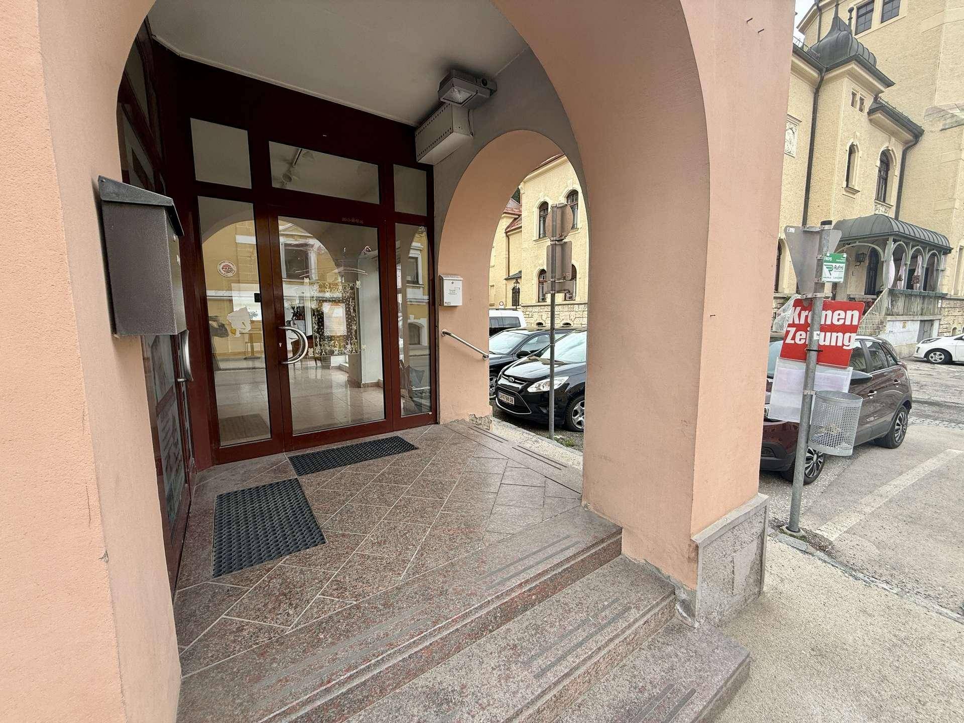 Gebäudeeingang mit bogenförmigem Portal, Glastüren und Granitstufen.