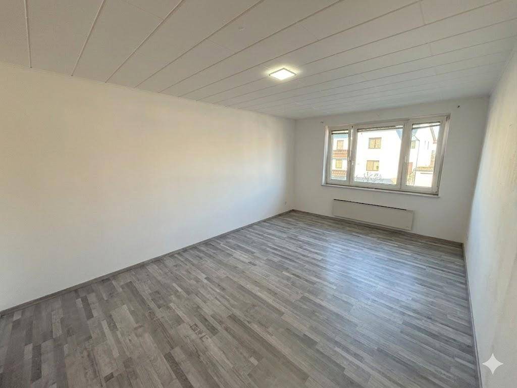 Lichtdurchflutetes Zimmer mit Laminatboden und einem großen Fenster, das viel Tageslicht hereinlässt.