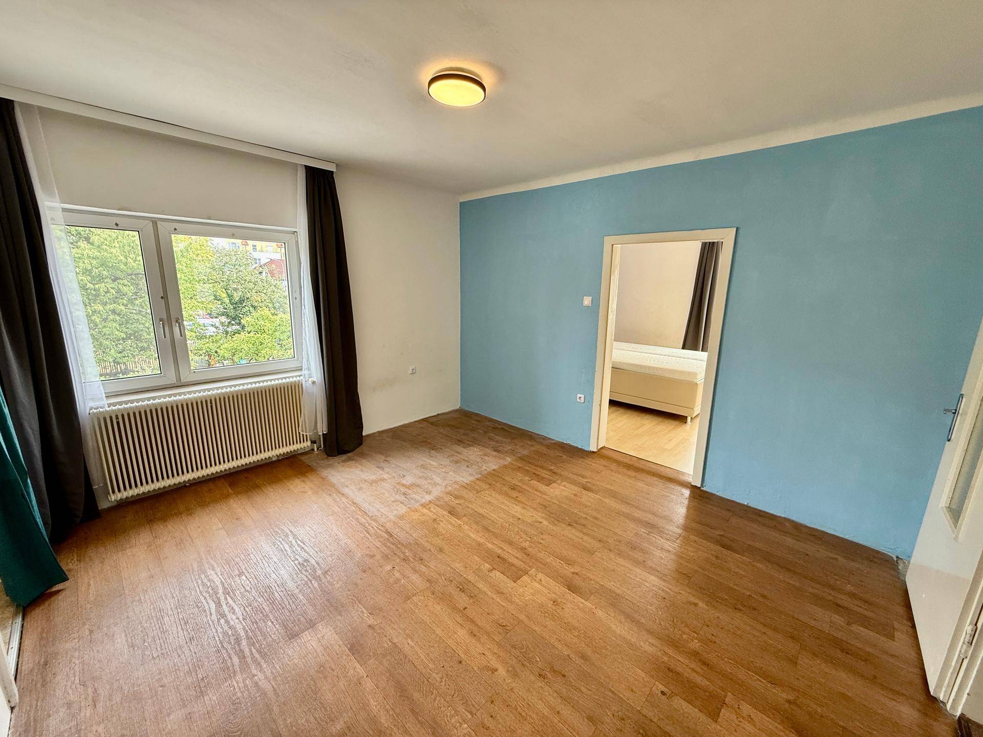 Geräumiges Schlafzimmer mit Holzboden und einer blauen Akzentwand, verbunden mit einem weiteren Raum.