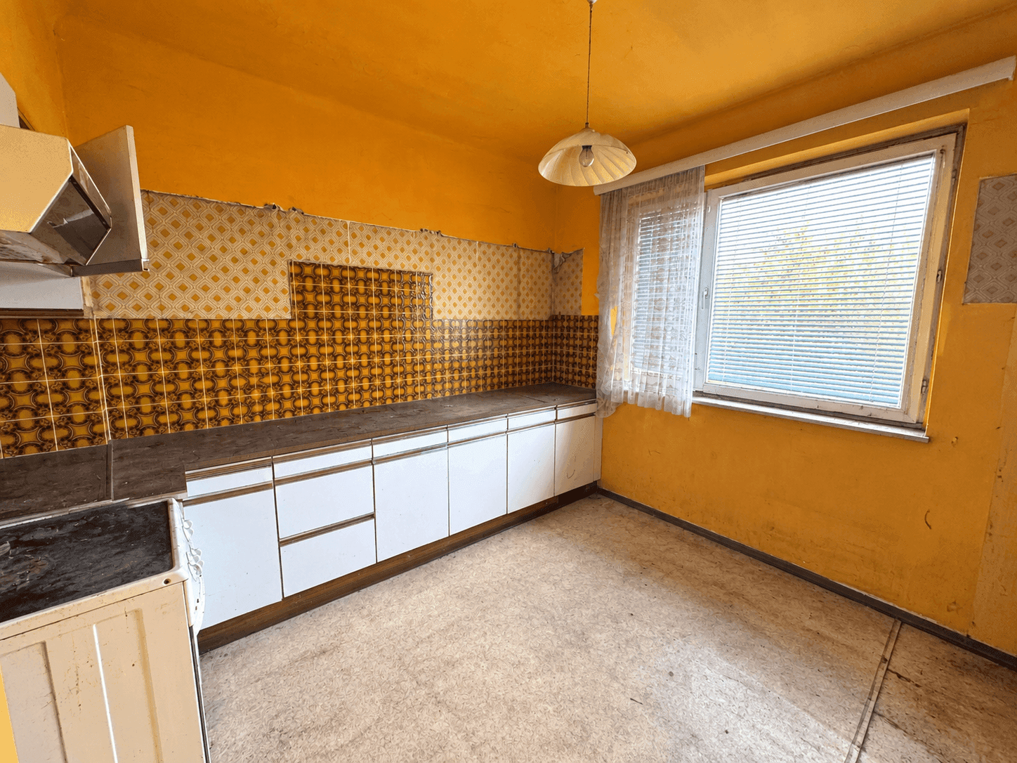 Renovierungsbedürftige Küche mit orangefarbenen Wänden, alten Fliesen und einfachen Unterschränken.