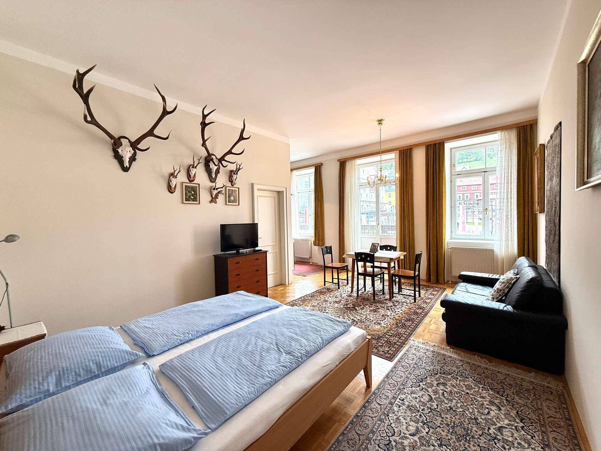 Heller Wohn- und Schlafbereich mit Parkettboden, Esstisch und Blick auf die Umgebung durch große Fenster.