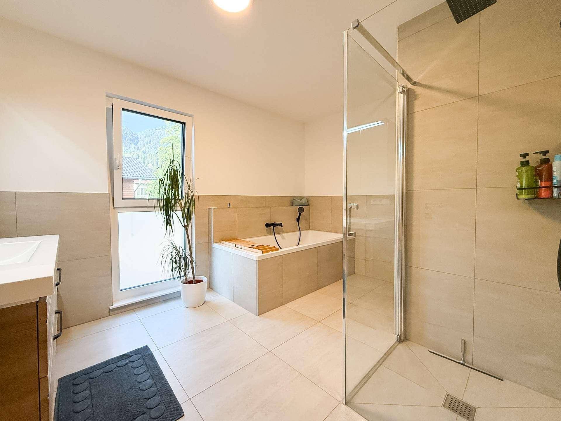 Geräumiges Badezimmer mit Badewanne, großer Dusche und Fenster.