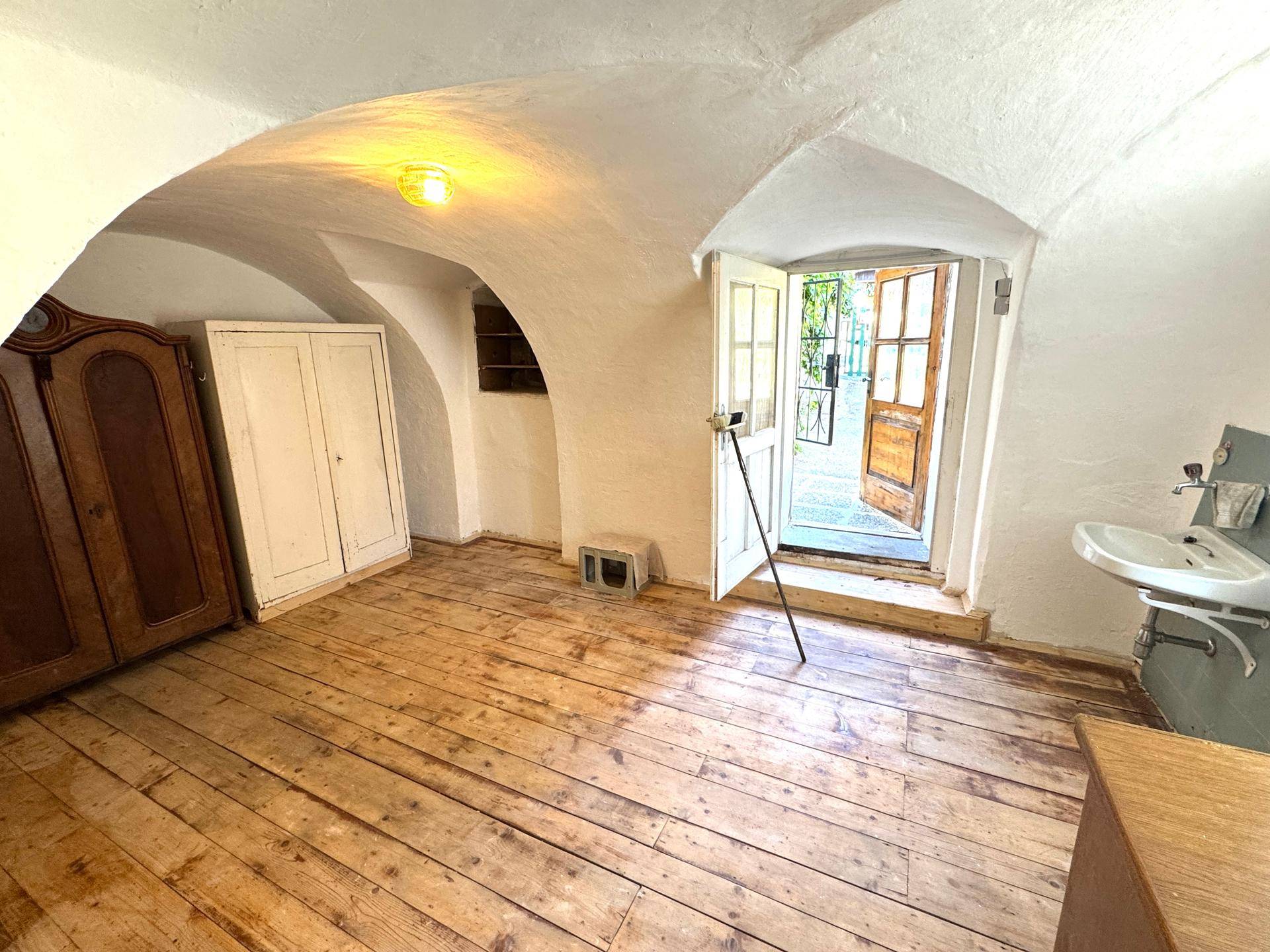 Historischer Kellerraum mit Gewölbedecke, Holzdielenboden und direktem Zugang nach draußen.