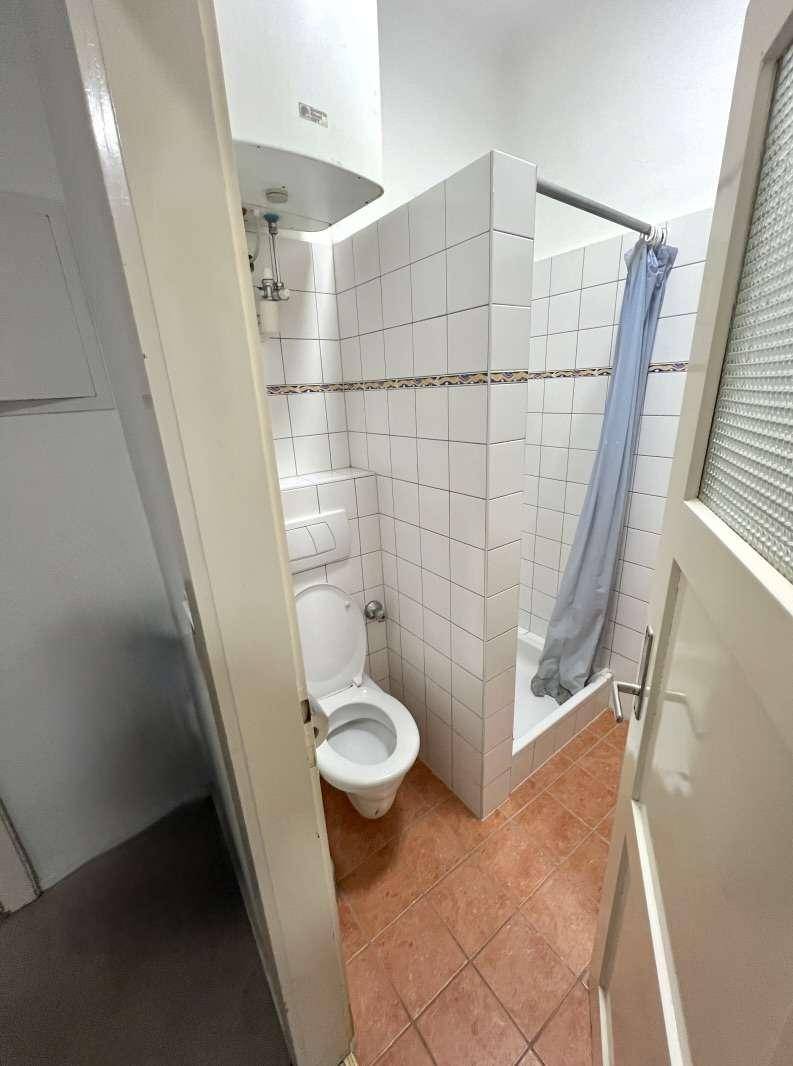 Kleines Badezimmer mit Dusche, WC und Warmwasserboiler, ausgestattet mit Fliesen.