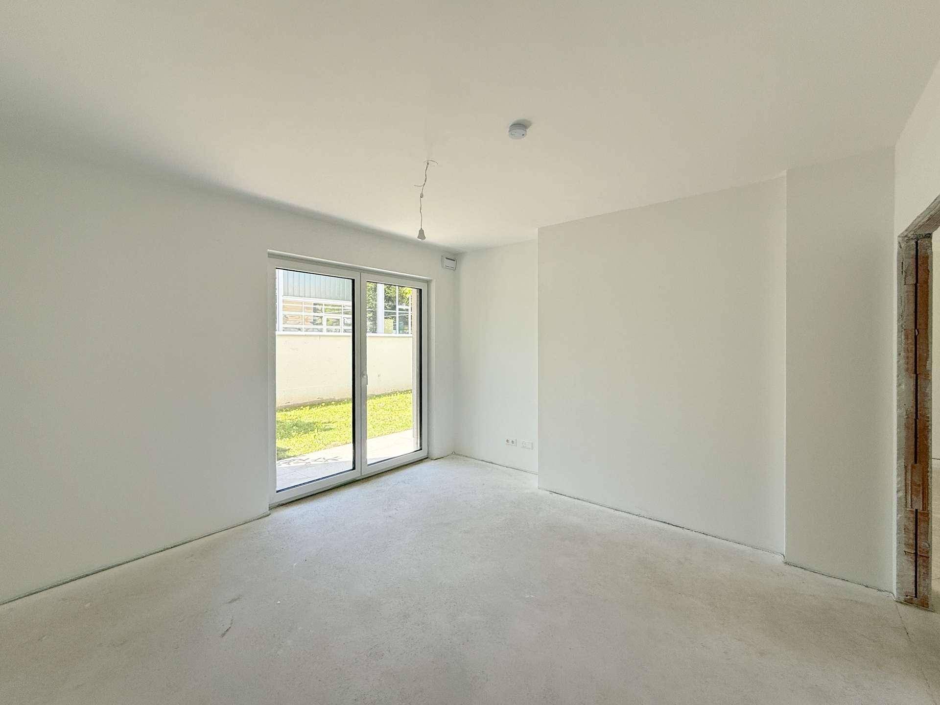 Unmöbliertes Zimmer mit viel Tageslicht und Schiebetür zum privaten Gartenbereich.