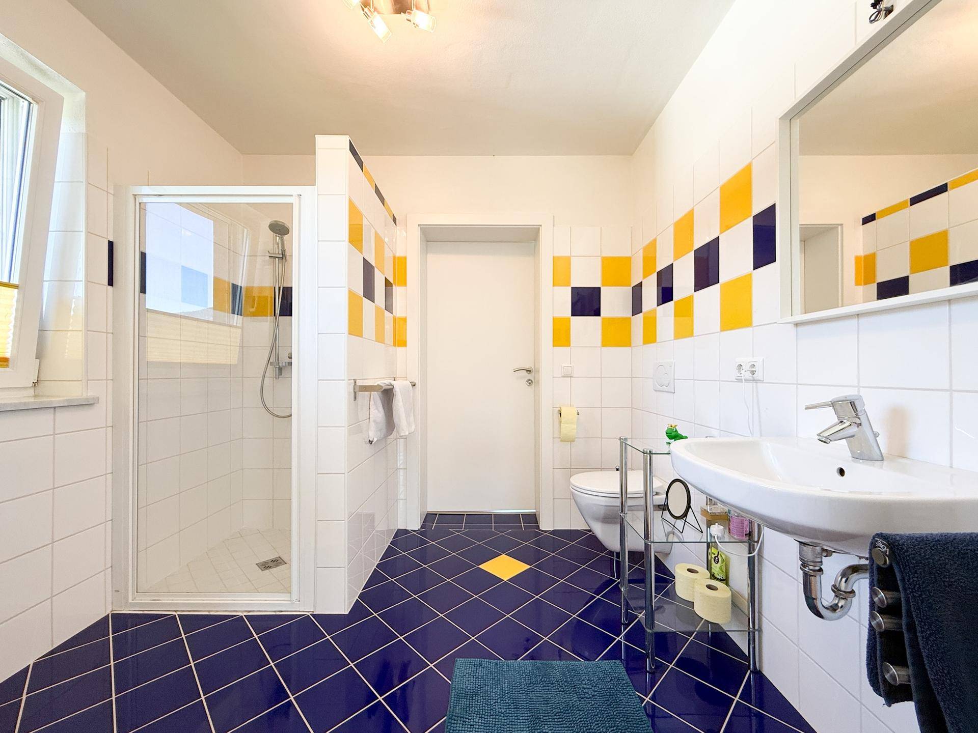 Buntes Badezimmer mit Dusche, blauen und gelben Fliesen und Einzelwaschbecken.