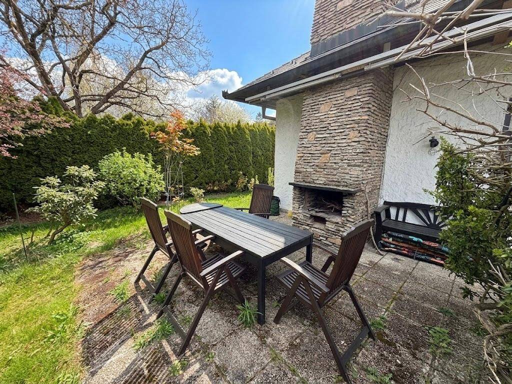 Gepflasterte Terrasse mit Esstisch, Stühlen und gemauertem Grillkamin im Garten.