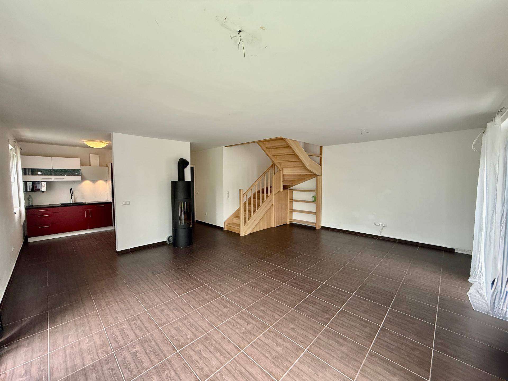 Offener Wohnbereich mit Kaminofen, Holztreppe und Blick auf die angrenzende Küche.
