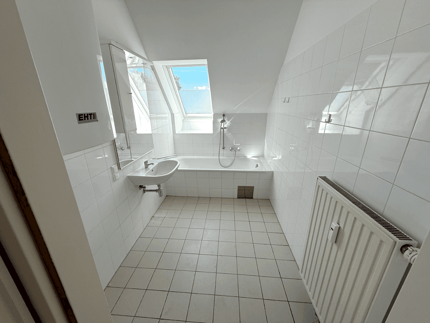 Helles Badezimmer mit weißen Fliesen, Badewanne, Waschbecken und einem Dachfenster.