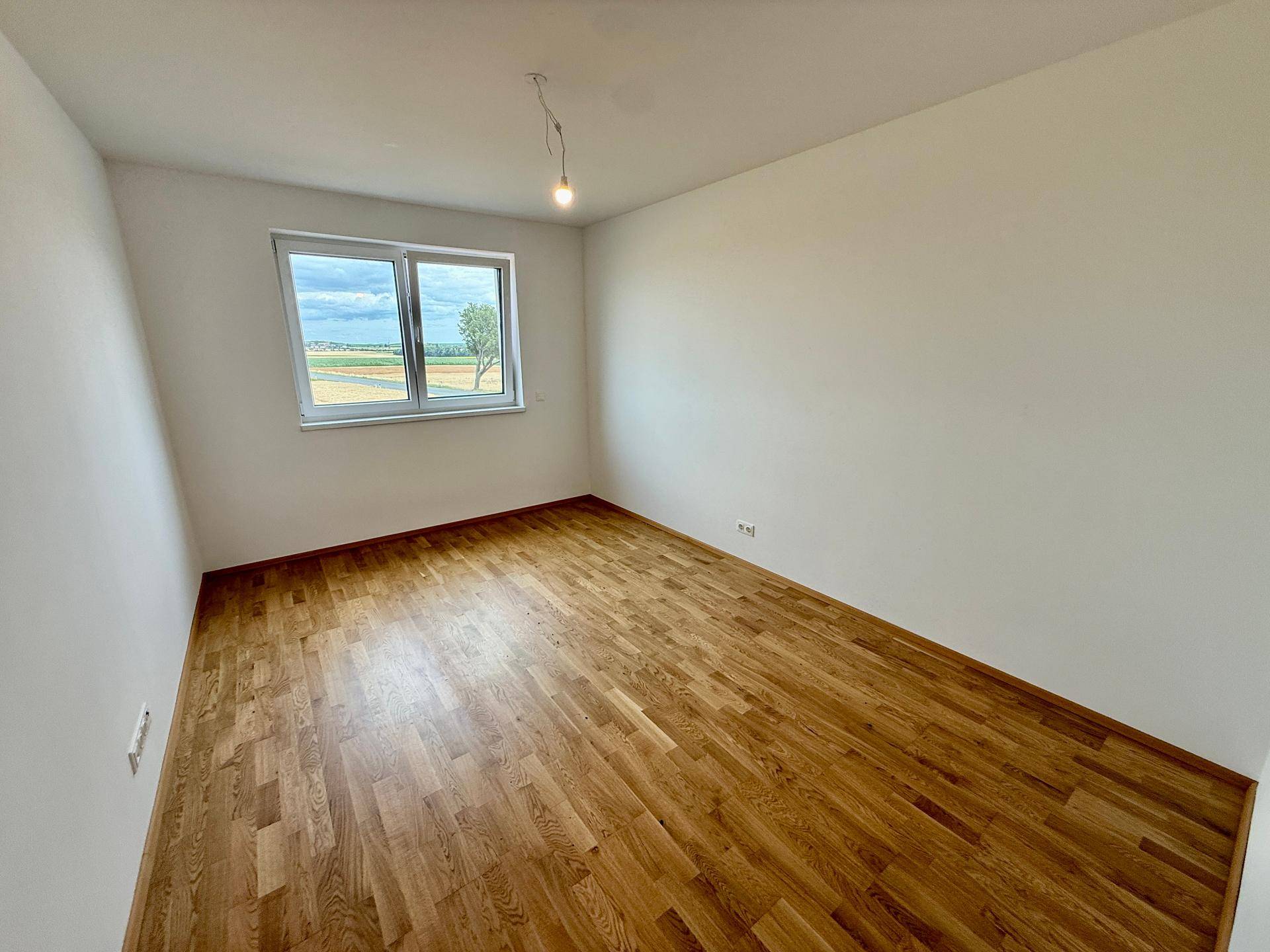 Lichtdurchflutetes Schlafzimmer mit Holzboden und Ausblick auf die umliegende Landschaft.