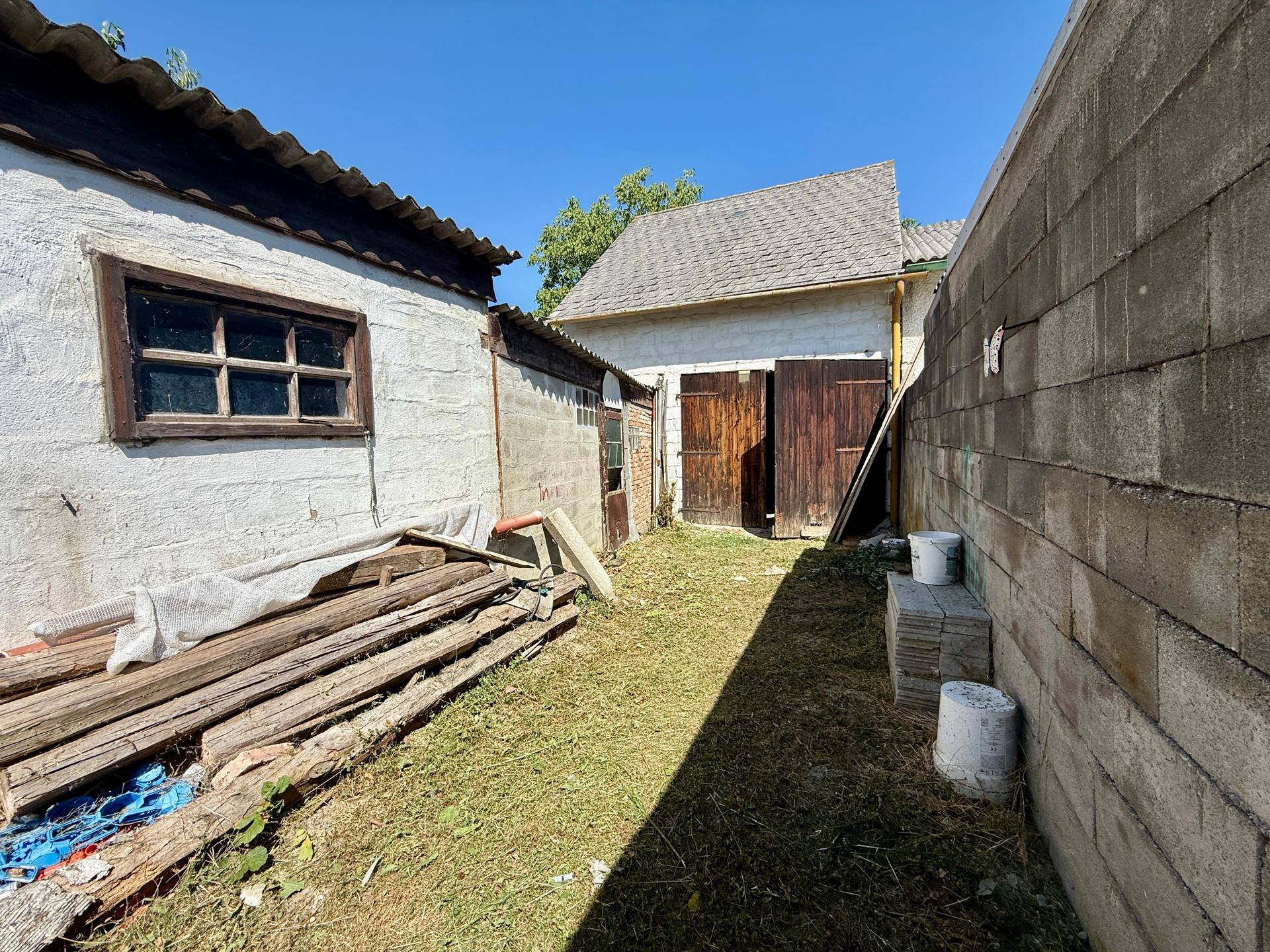 Ländlicher Hinterhof mit alten Nebengebäuden, Holztüren und einer Betonmauer.