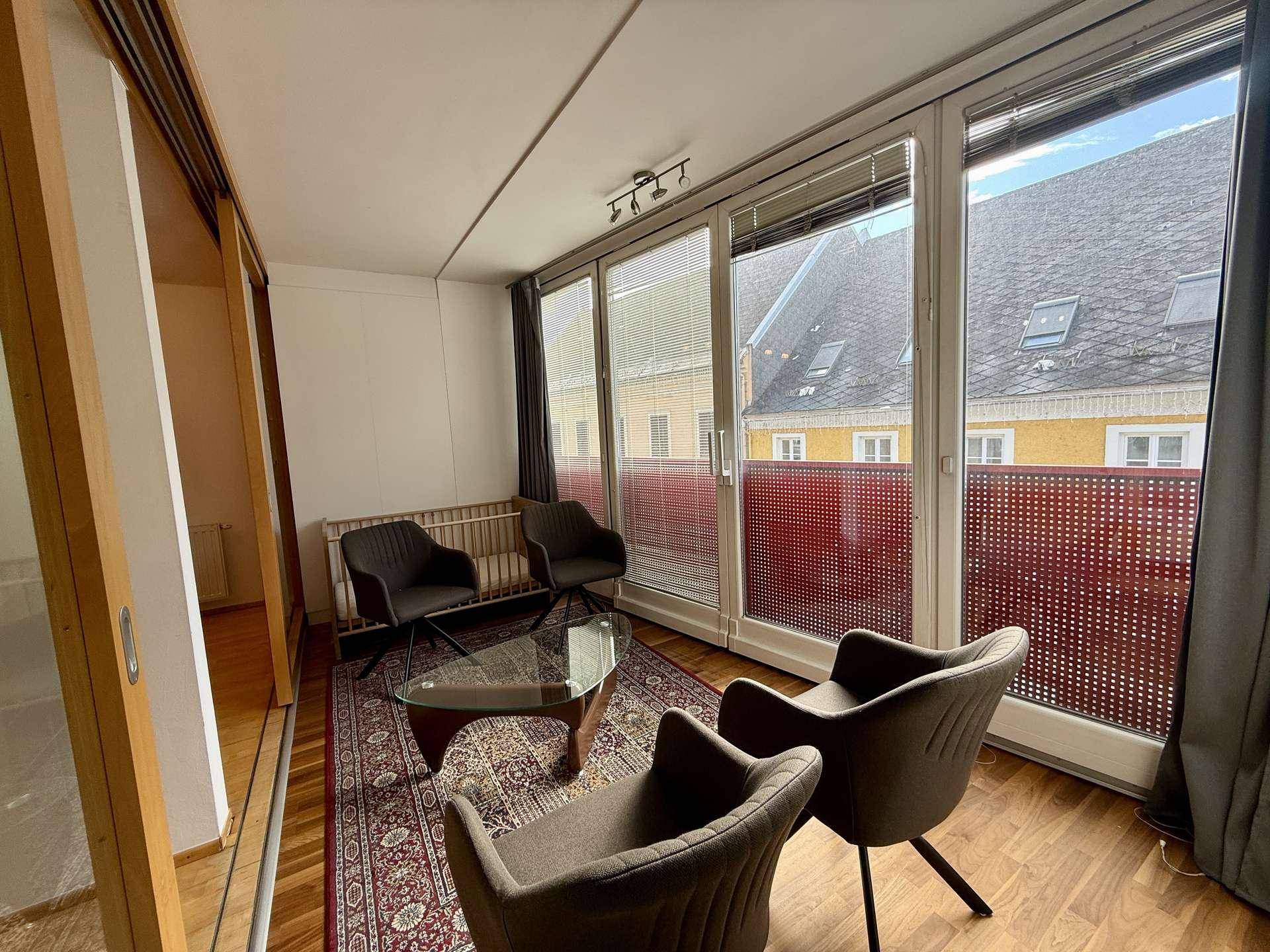 Verglaste Loggia mit Sitzgelegenheiten, Teppich und Blick auf die umliegenden Dächer.