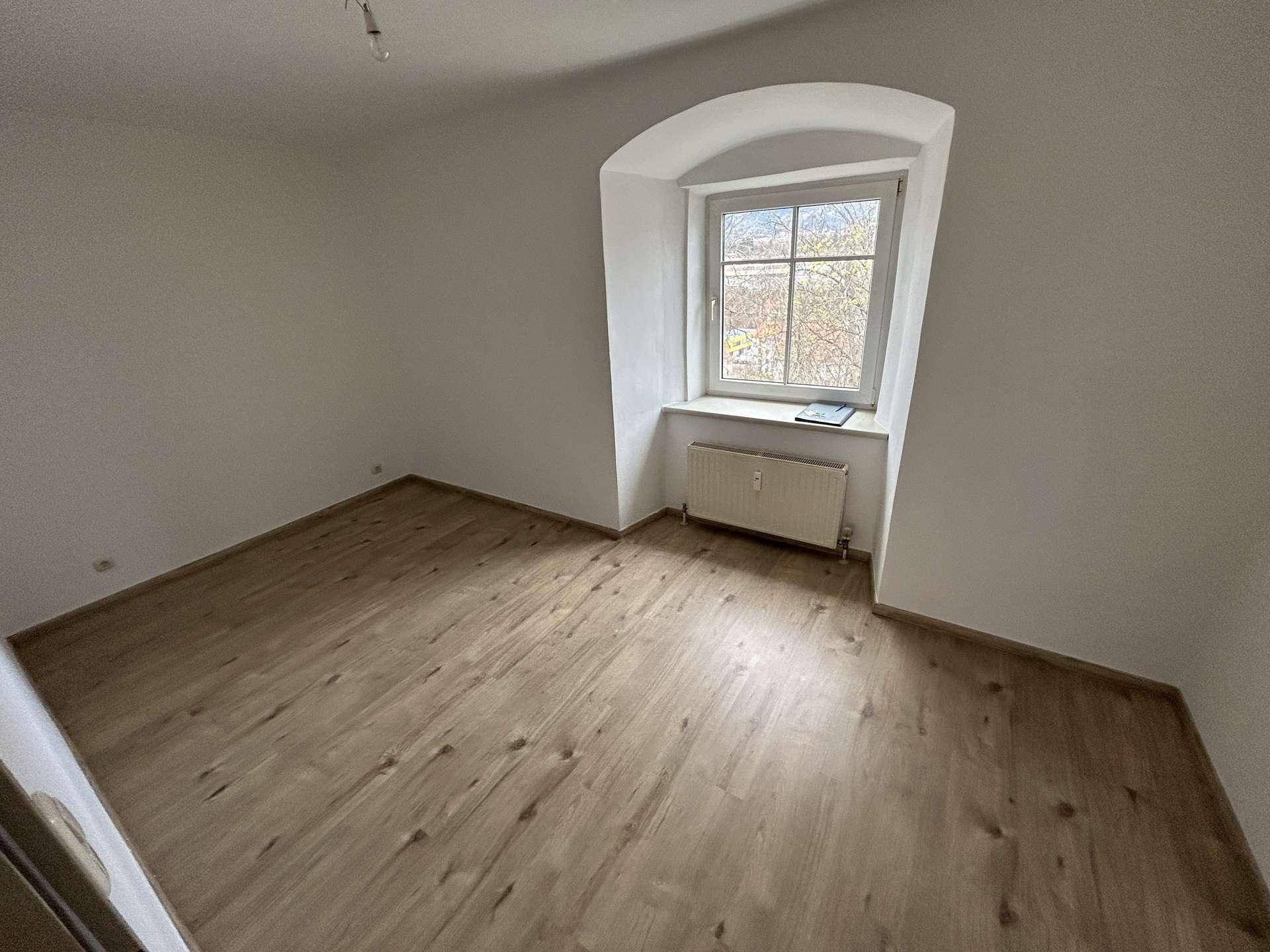 Helles Zimmer mit Laminatboden und einem charmanten, gewölbten Fenster, das viel Licht hereinlässt.