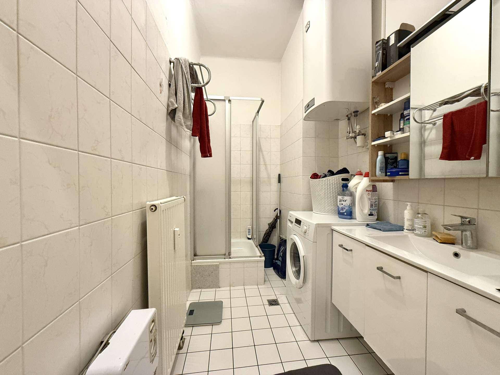 Gefliestes Badezimmer mit Dusche, Waschbecken, Waschmaschine und Heizkörper.