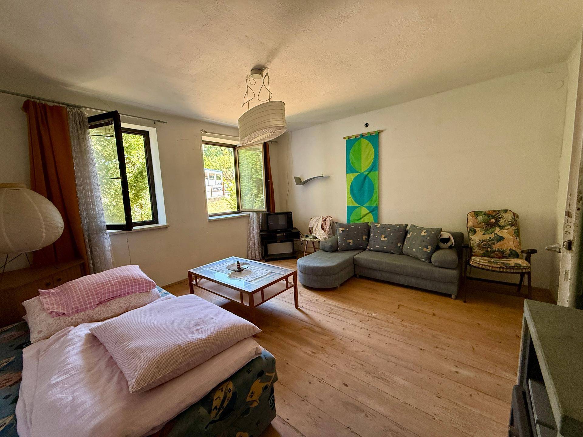 Helles Wohnzimmer mit Holzboden, Sofa und Blick ins Grüne durch die Fenster.