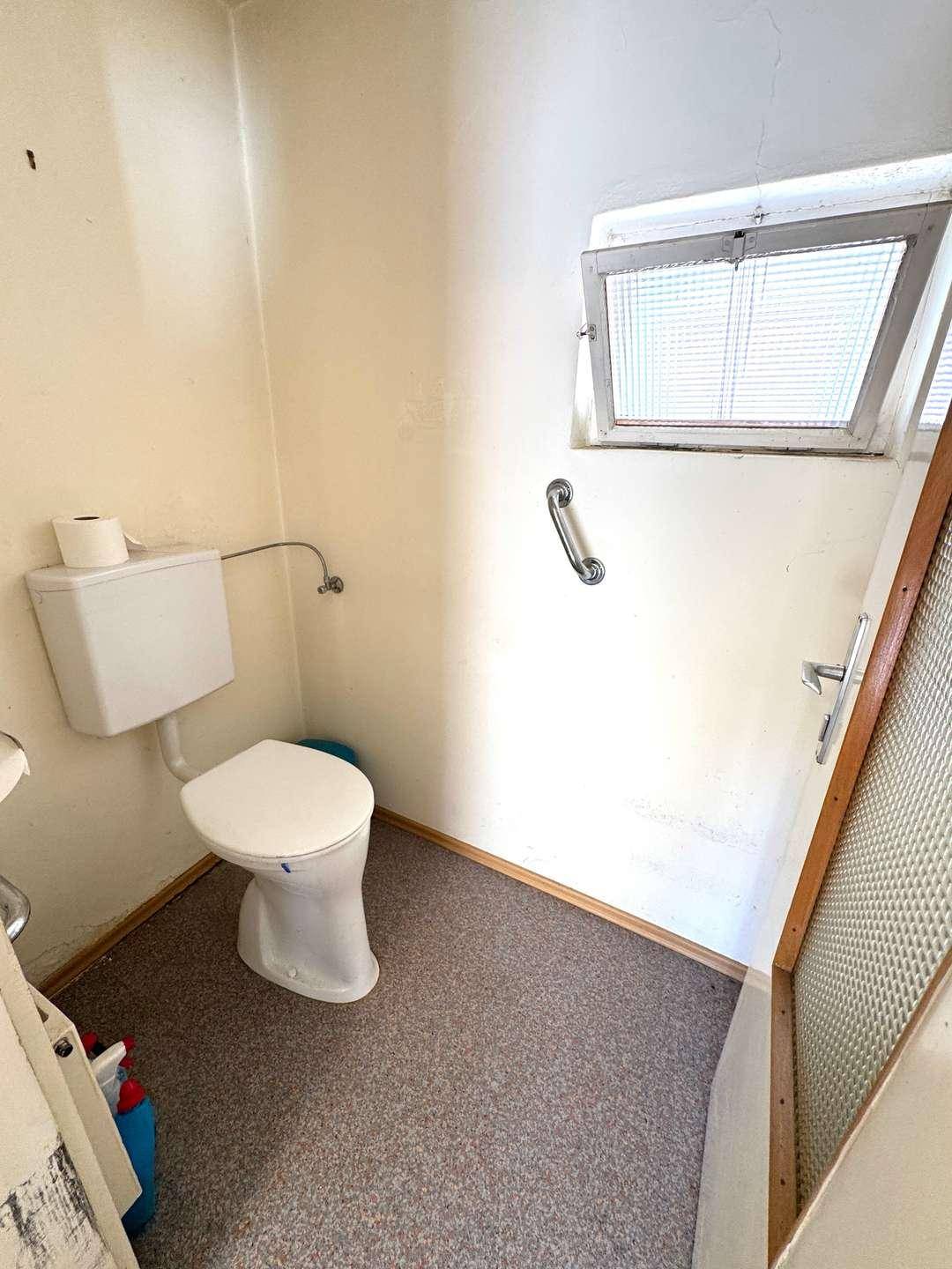 Kleines WC mit Fenster, Toilette und Haltegriff für zusätzliche Sicherheit.