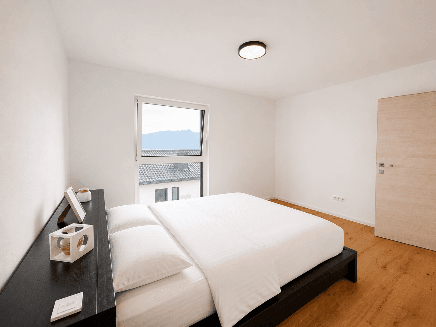 Helles Schlafzimmer mit Holzboden, modernem Bett und Fenster mit Bergblick.