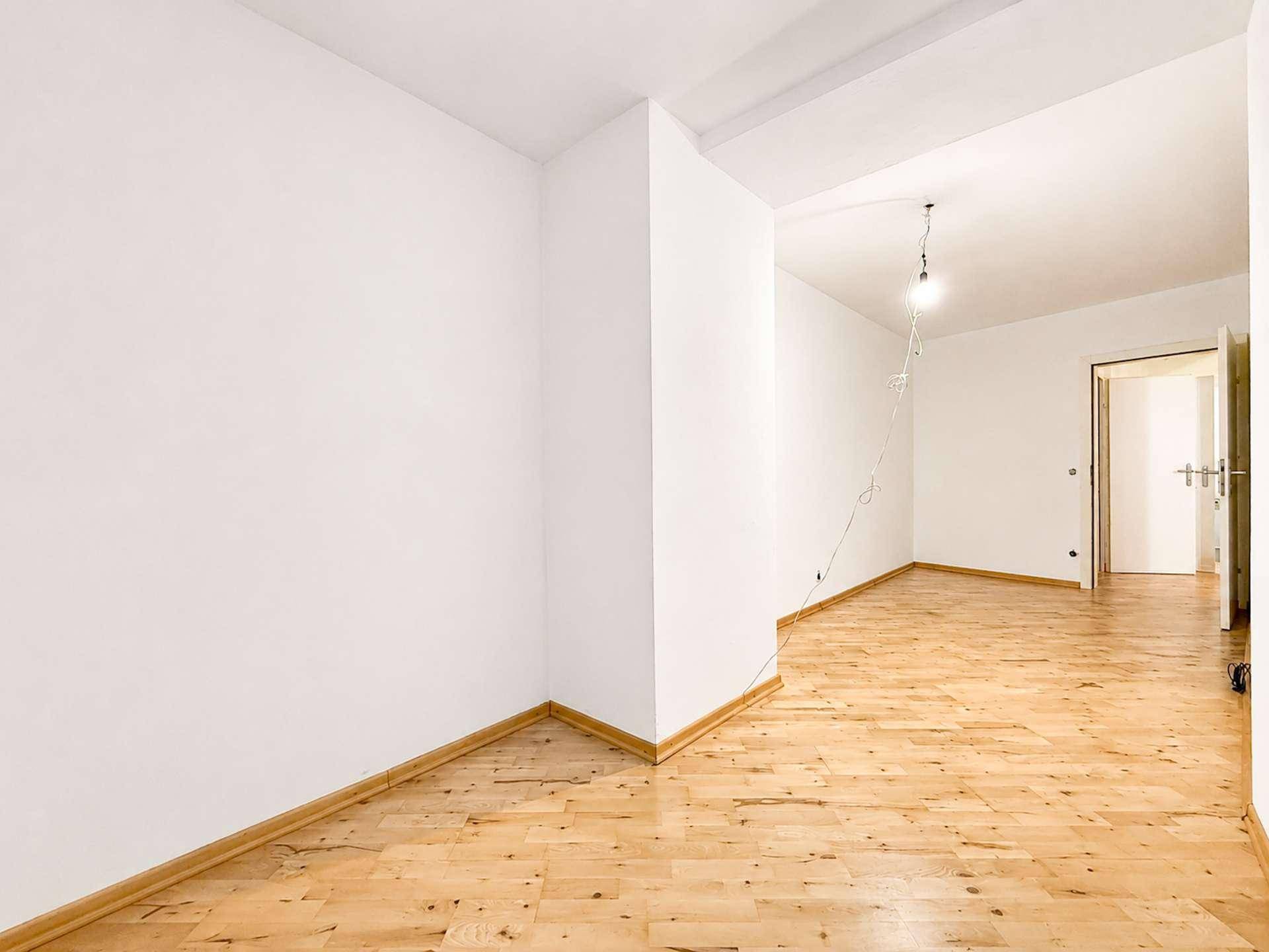 Heller Raum mit Holzboden und weiß gestrichenen Wänden, bietet Zugang zu weiteren Bereichen.