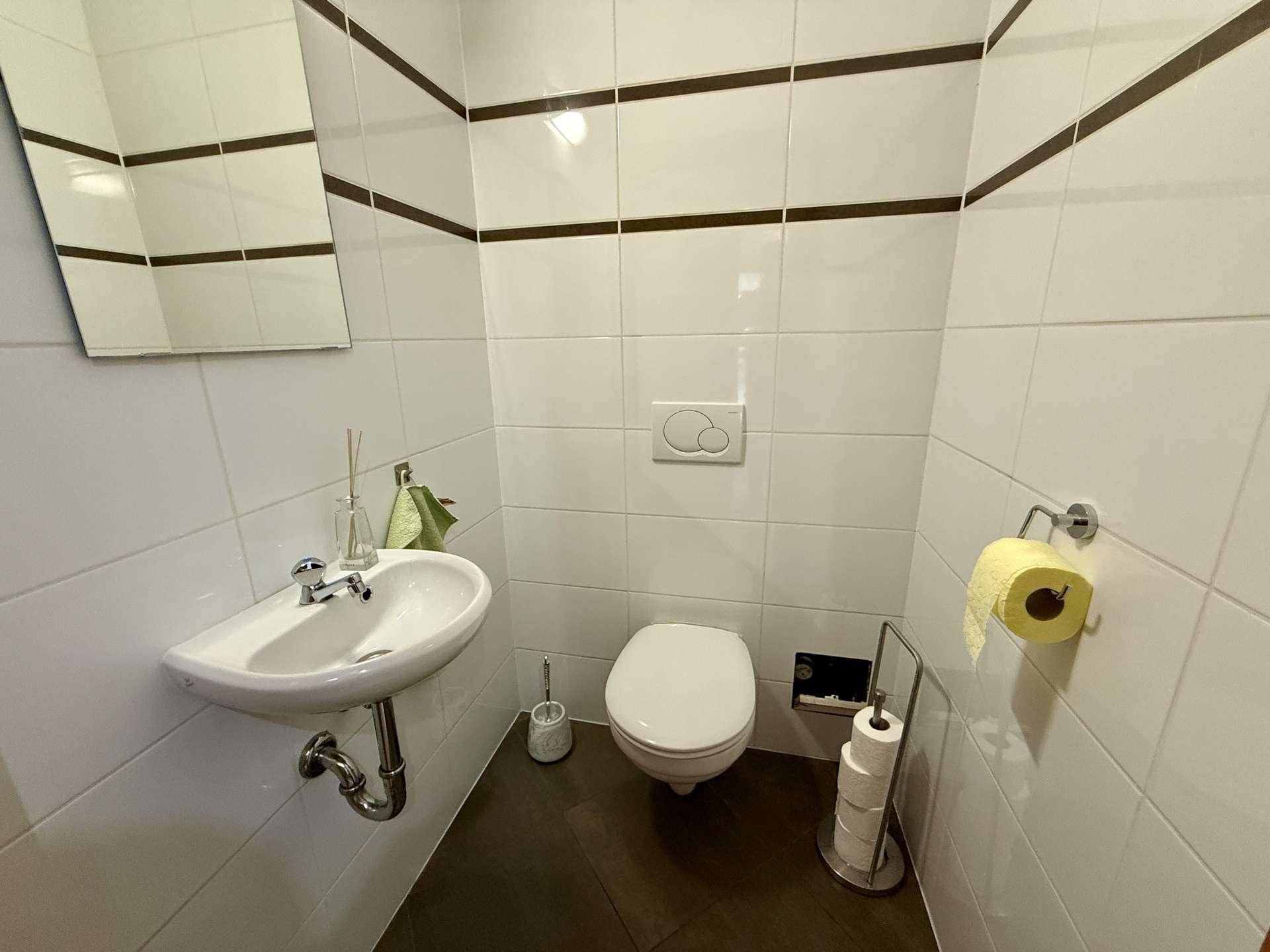 Kleines Gäste-WC mit weißen Fliesen, wandhängendem WC und modernem Waschbecken.