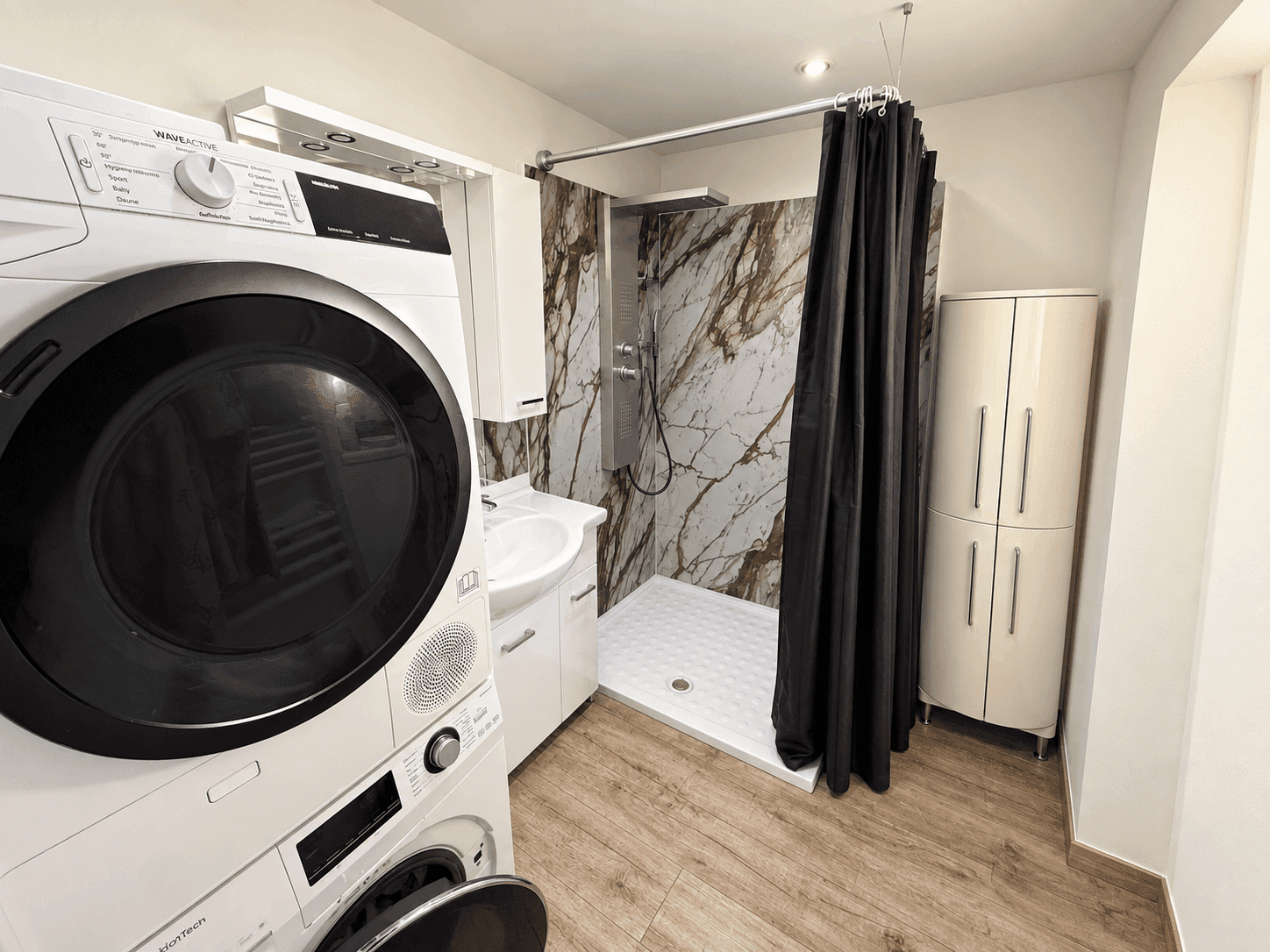 Modernes Badezimmer mit Dusche, Waschmaschine, Trockner und Marmor-Effekt-Wandpaneelen.