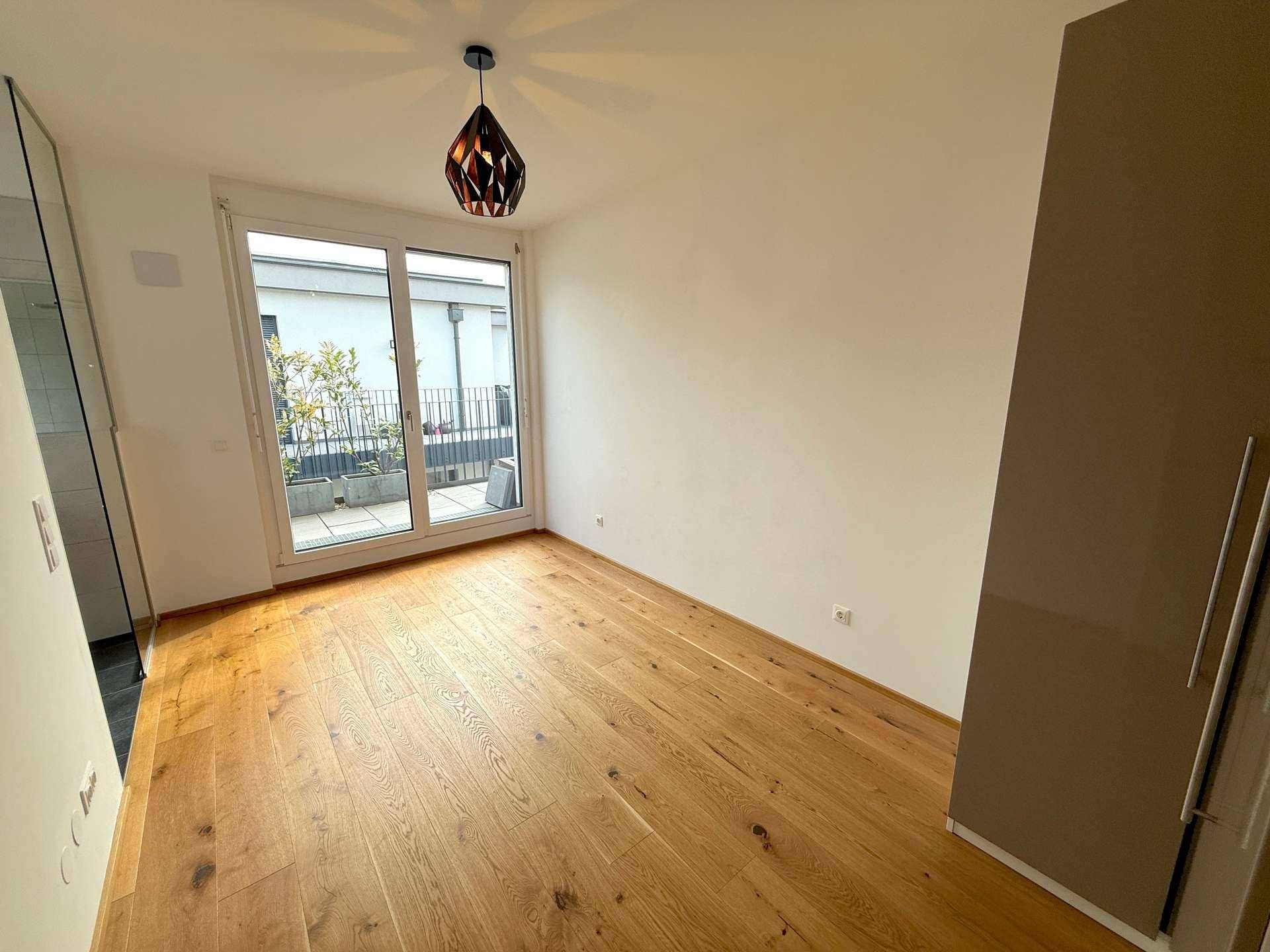 Helles Schlafzimmer mit Holzboden und großer Glastür, die zu einem Außenbereich führt.
