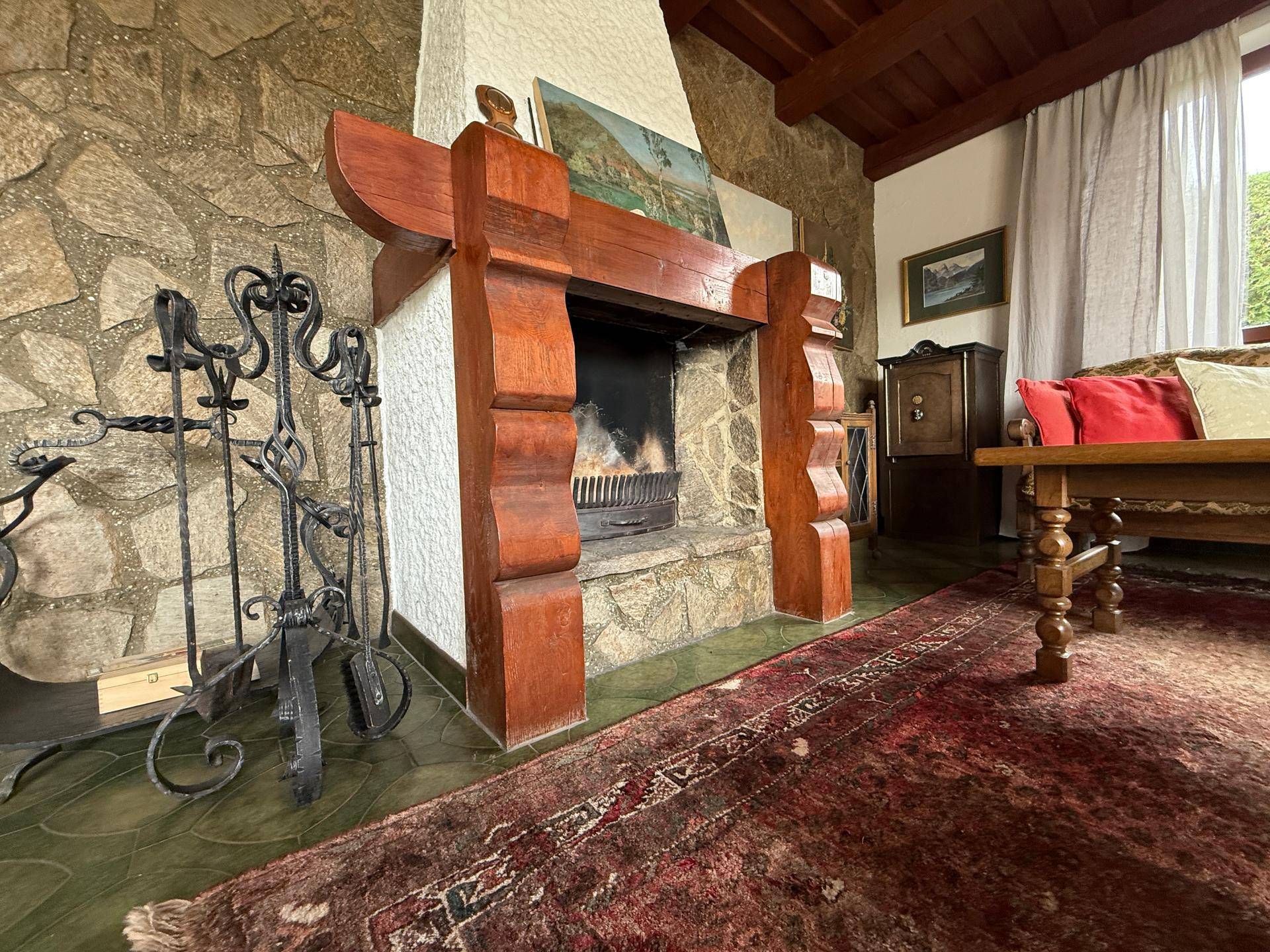Detailansicht des rustikalen Steinkamins mit Holzeinfassung und traditionellem Teppich im Wohnzimmer.