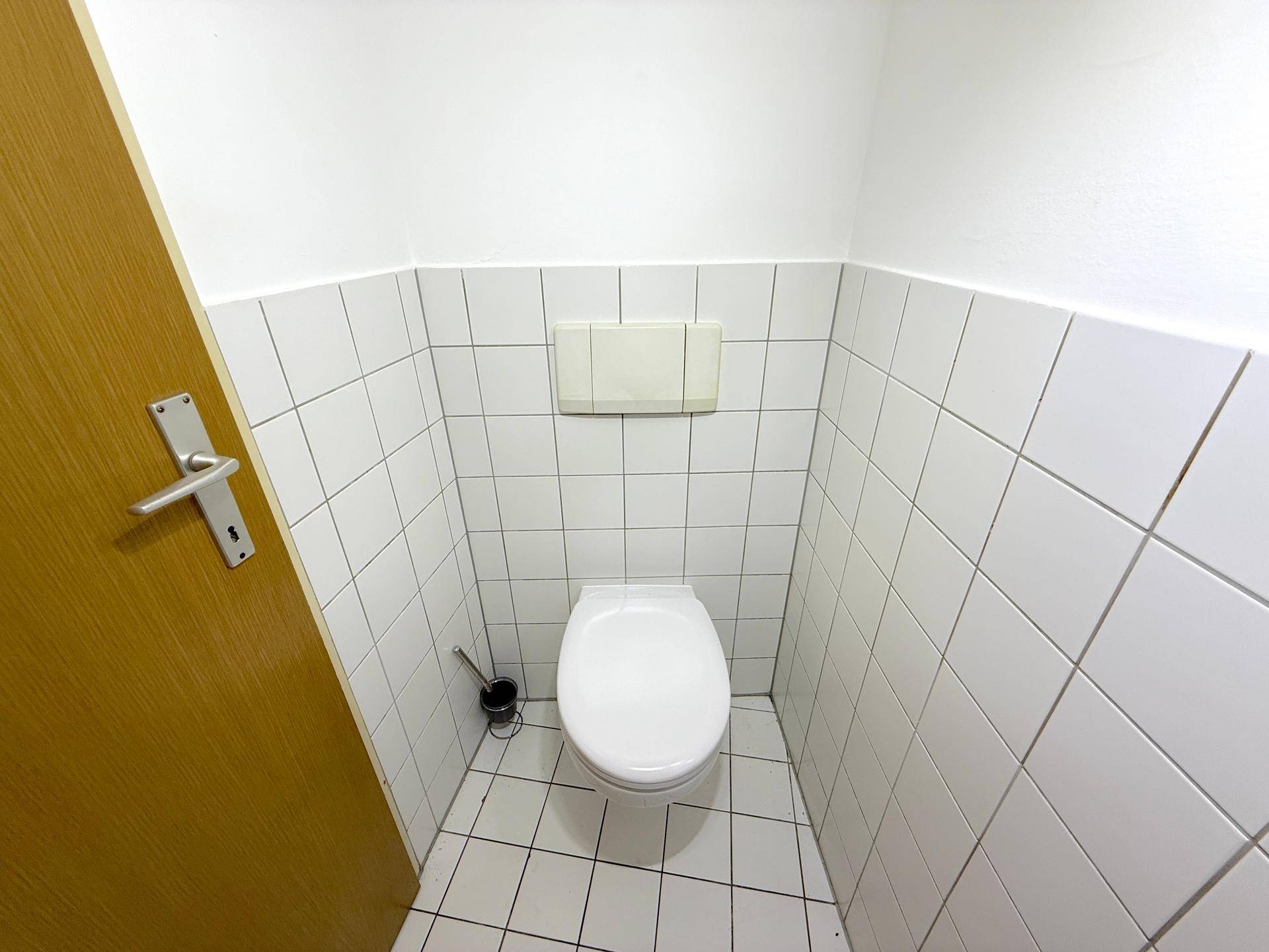 Kleines separates WC mit weißen Fliesen an Wänden und Boden.