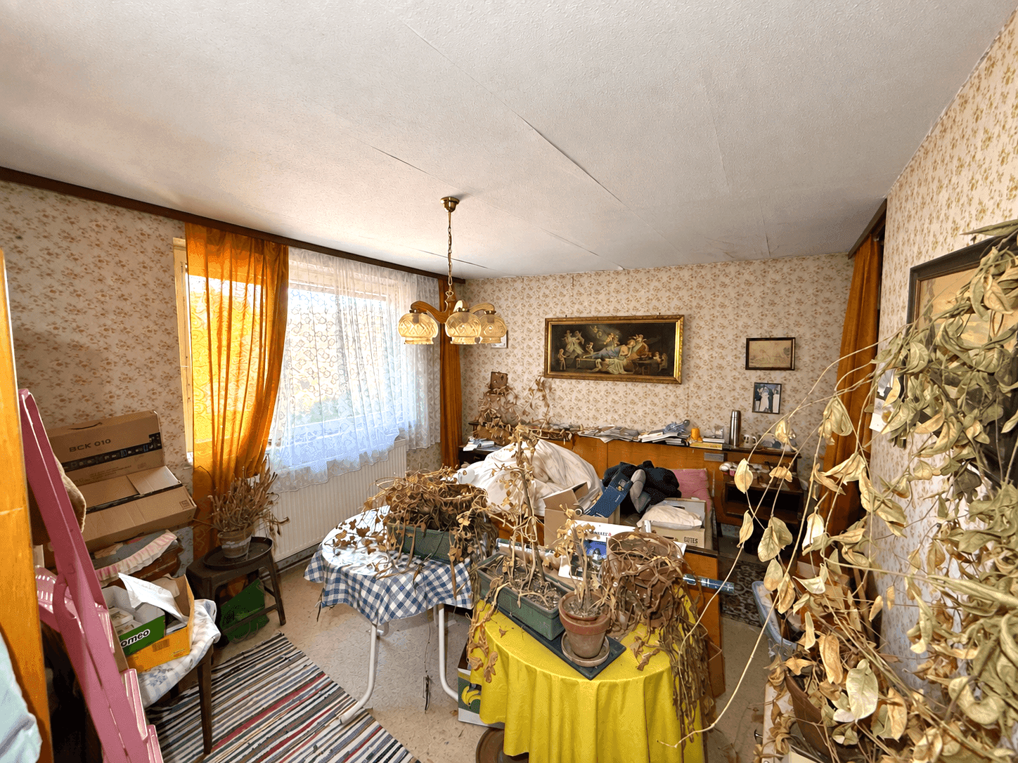 Schlafzimmer mit Bett, floraler Tapete und Fenster mit Vorhängen, viele Pflanzen.