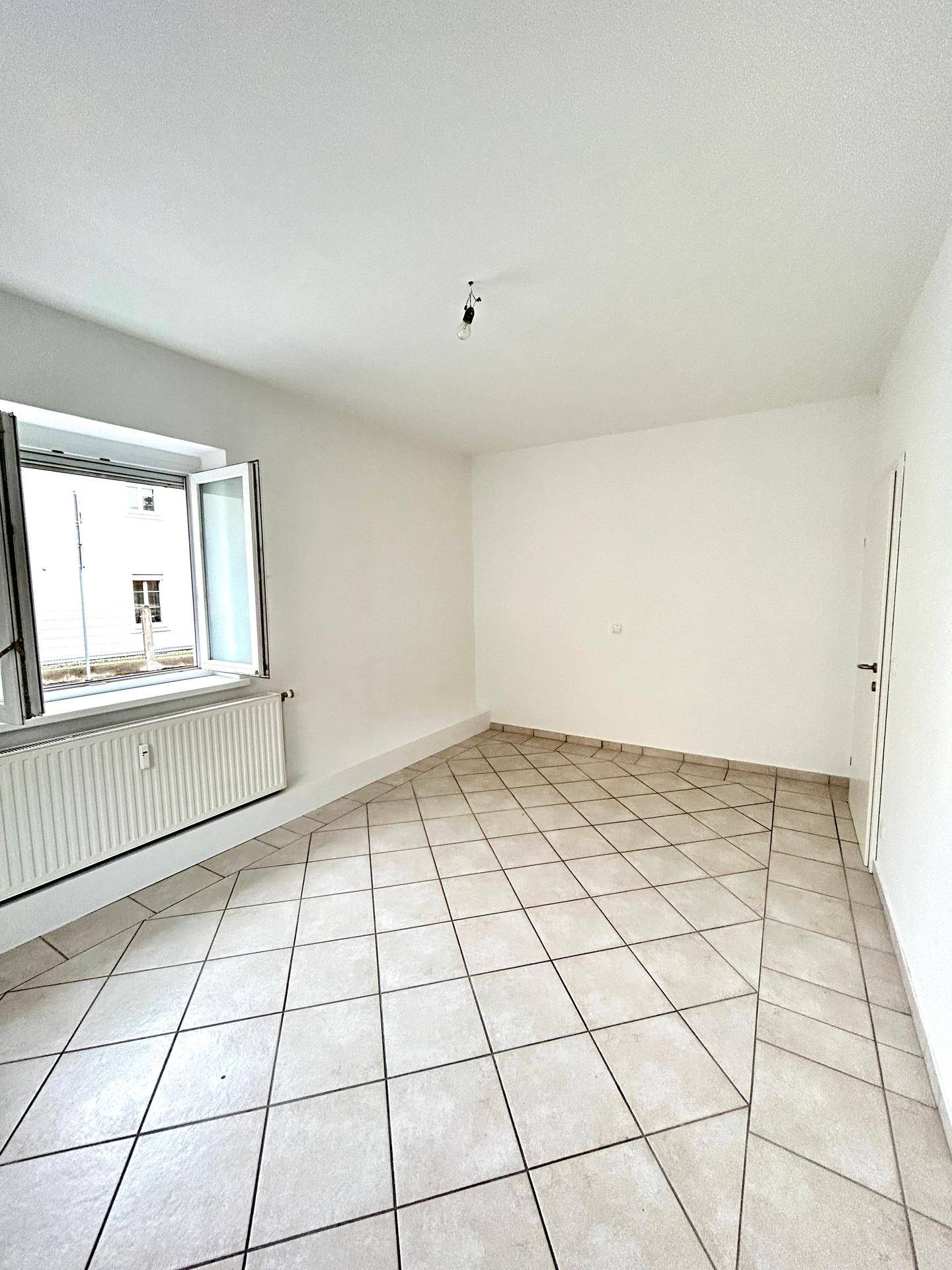 Heller Raum mit geöffnetem Fenster, Fliesenboden und Heizkörper unter dem Fenster.
