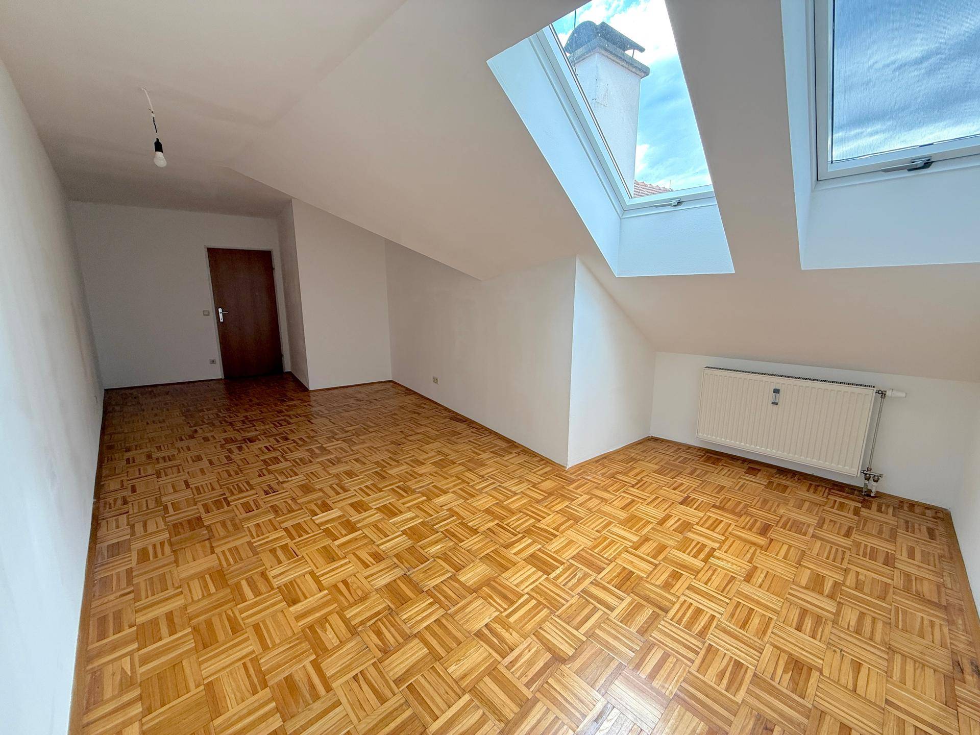Heller Dachgeschossraum mit Parkettboden, schrägen Wänden und Dachfenstern für viel Licht.