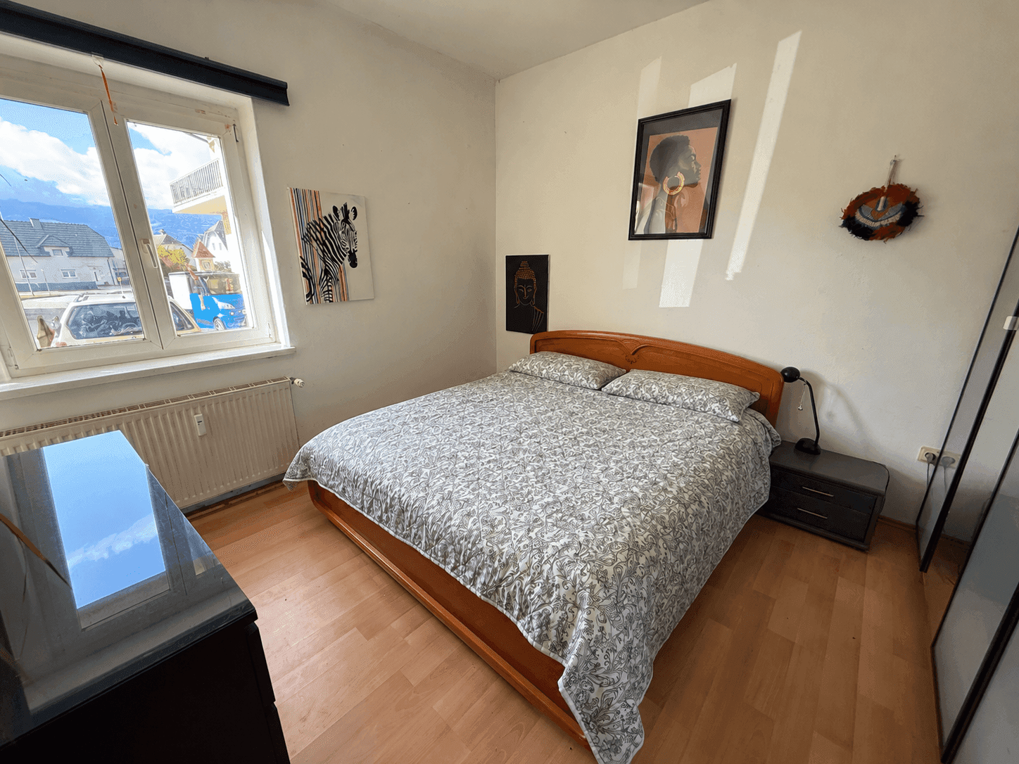 Helles Schlafzimmer mit Holzbett, Parkettboden und Blick ins Grüne durch das Fenster.