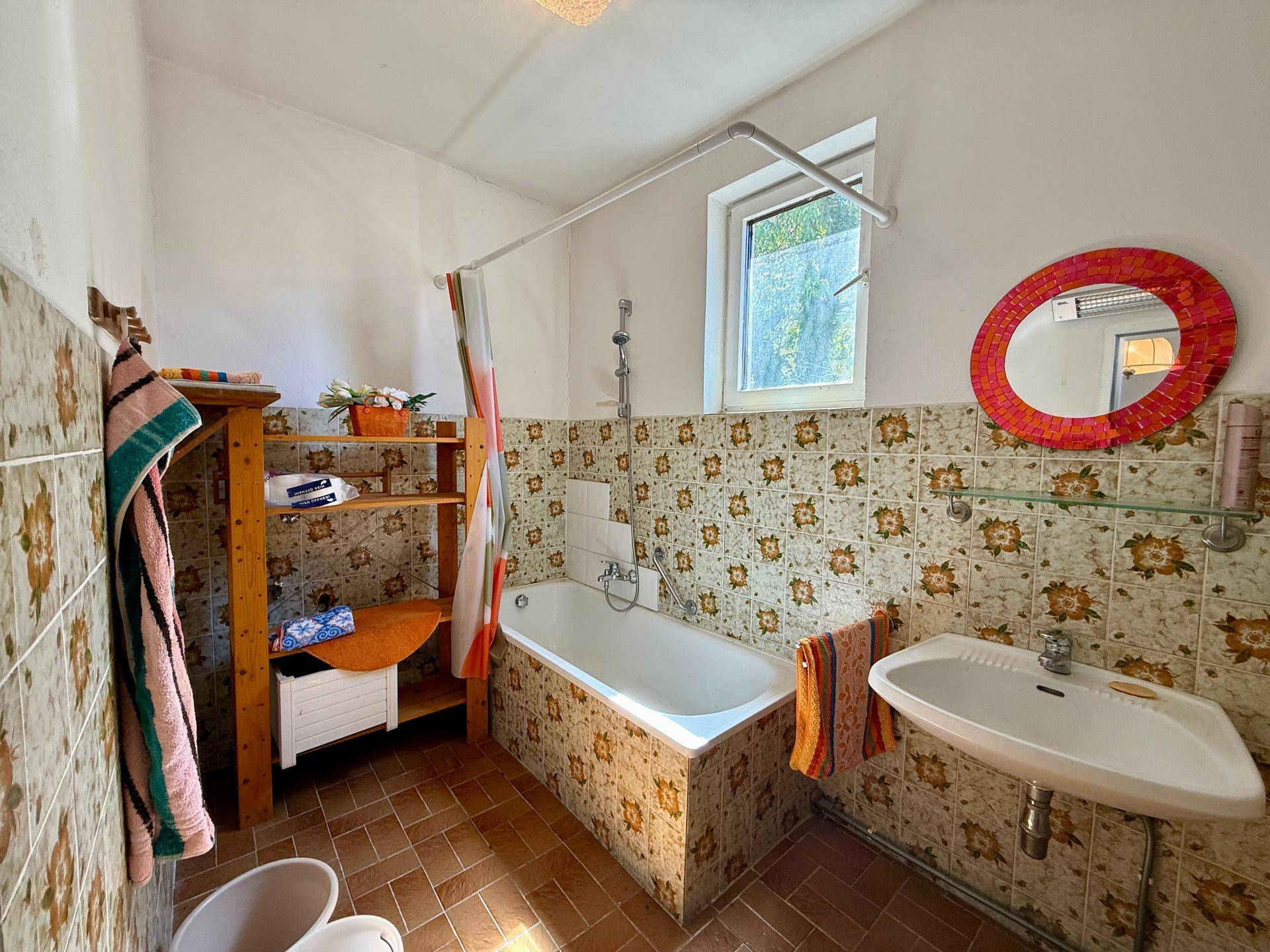 Badezimmer mit Badewanne, Waschbecken und charakteristischen Fliesen im Retro-Stil.