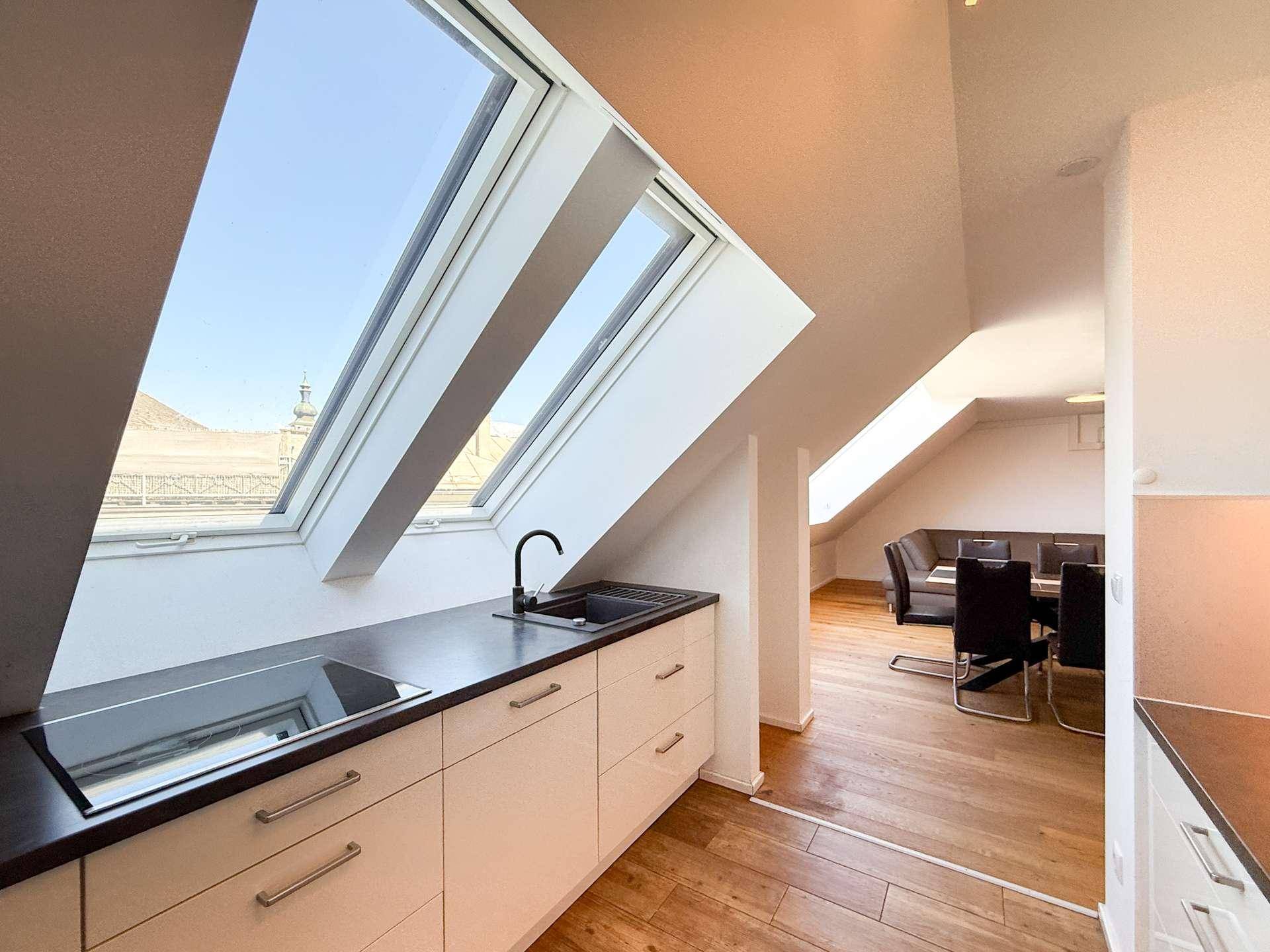 Funktionale Küche mit integriertem Kochfeld unter einem Dachfenster und Blick in den Wohnbereich.