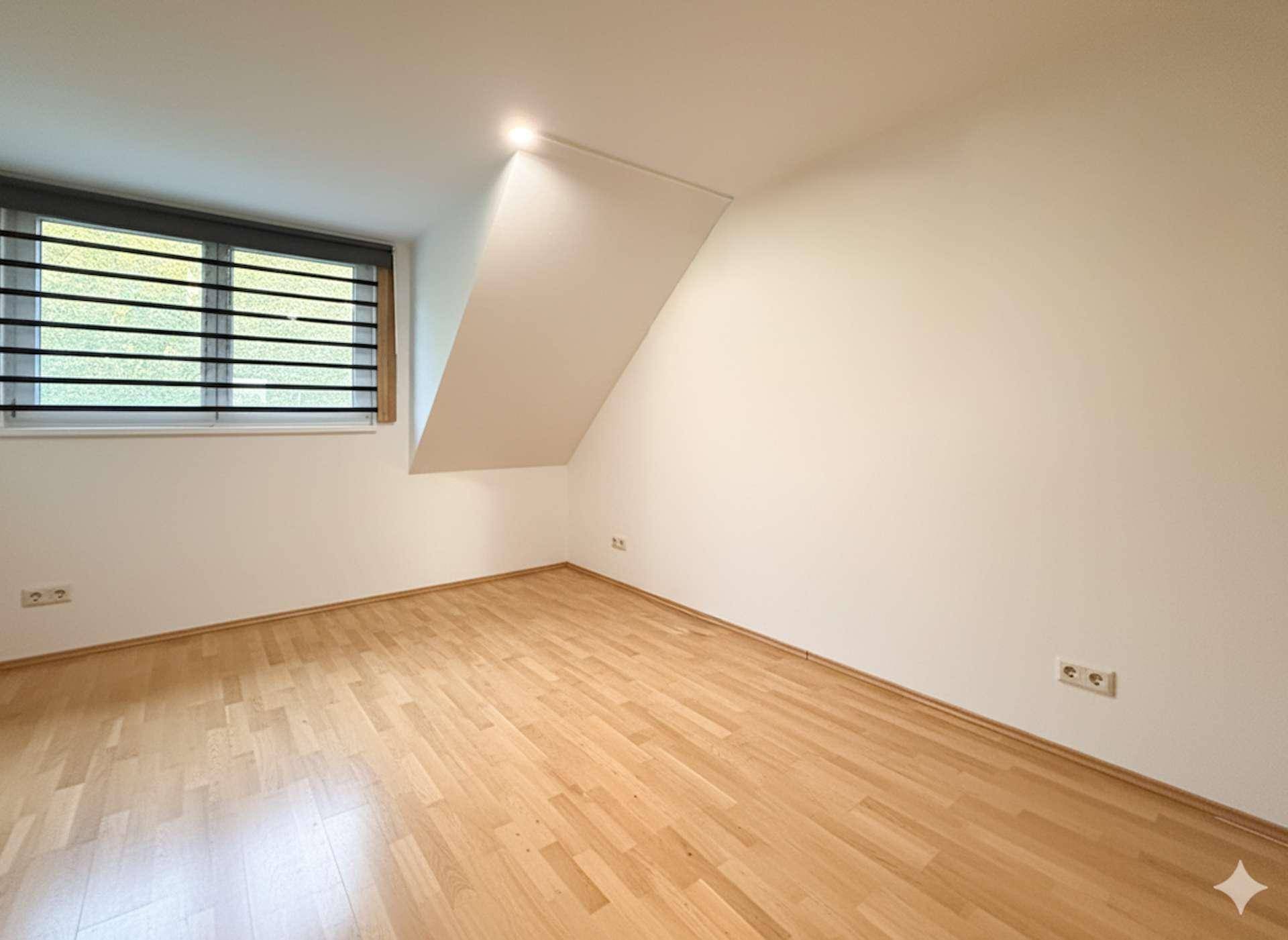 Leeres Zimmer mit Holzboden, Dachschräge und Fenster, bereit zur Einrichtung.